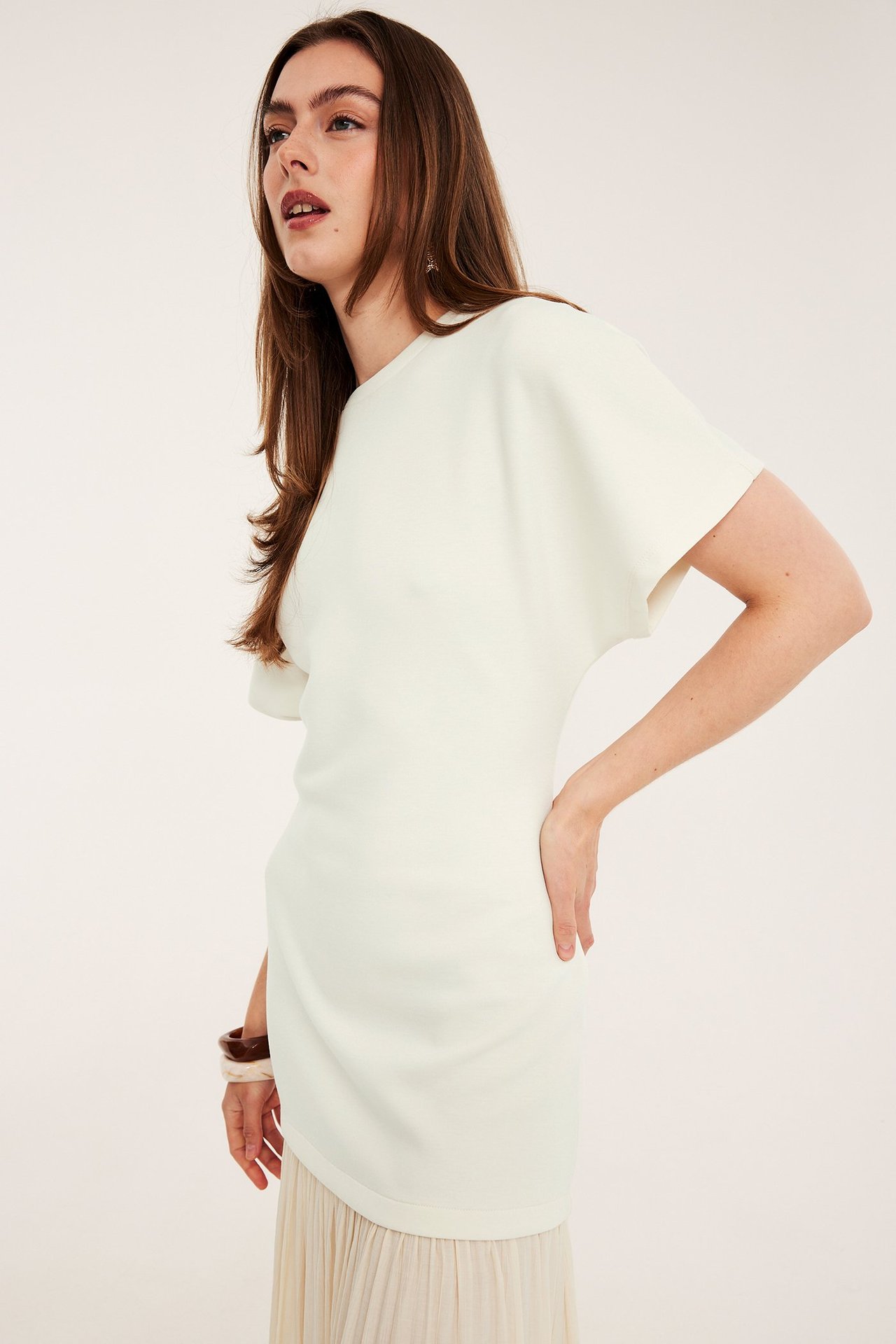 Nainen sivulta/edestä offwhite pitkässä mekossa, jossa lyhyet hihat, laskostettu hame ja rannekorut.