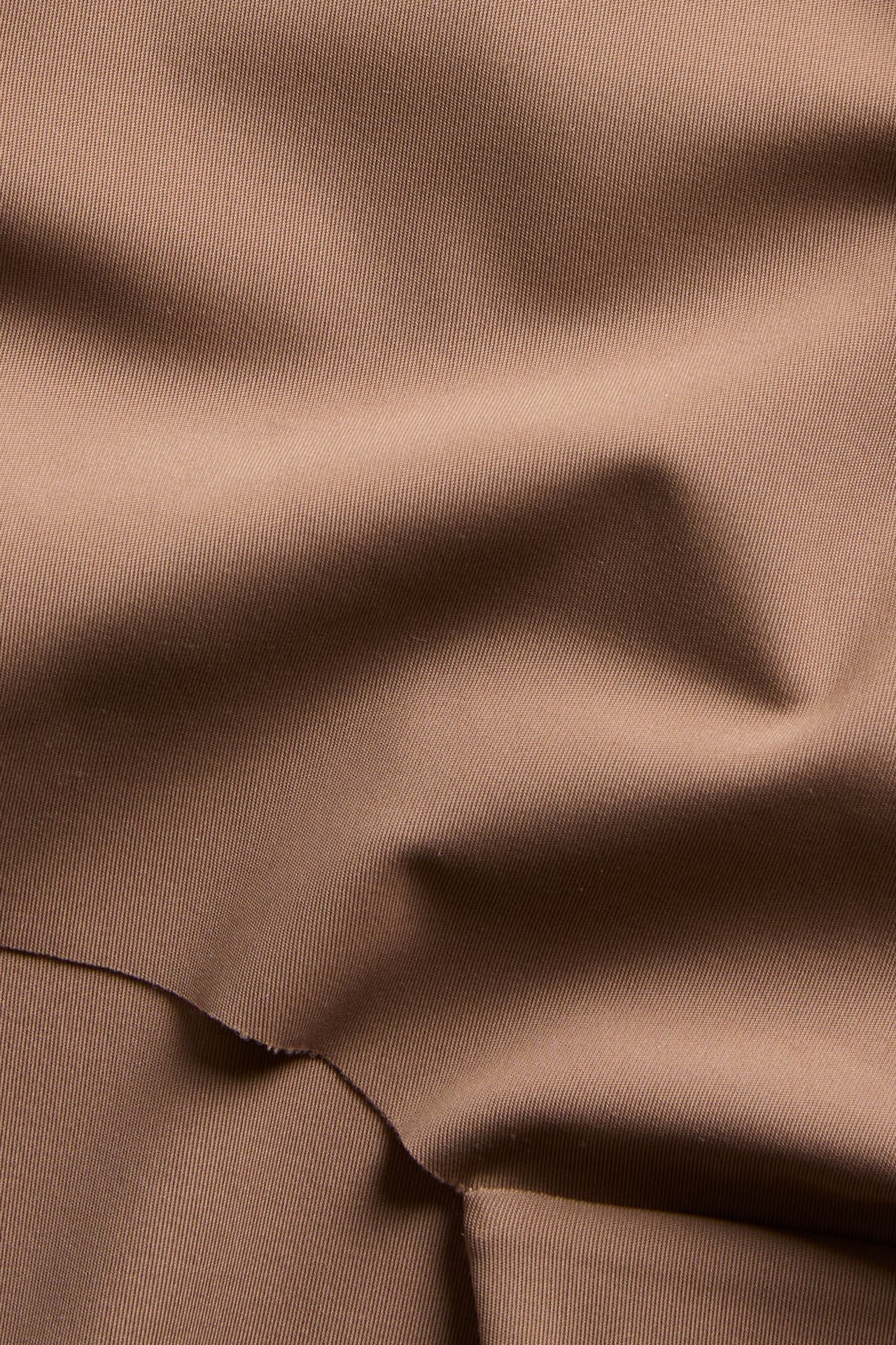 Lähikuva ruskeasta, yksivärisestä mikrokankaasta hipstertrosaan, jossa on hieno rakenne ja taitoksia.