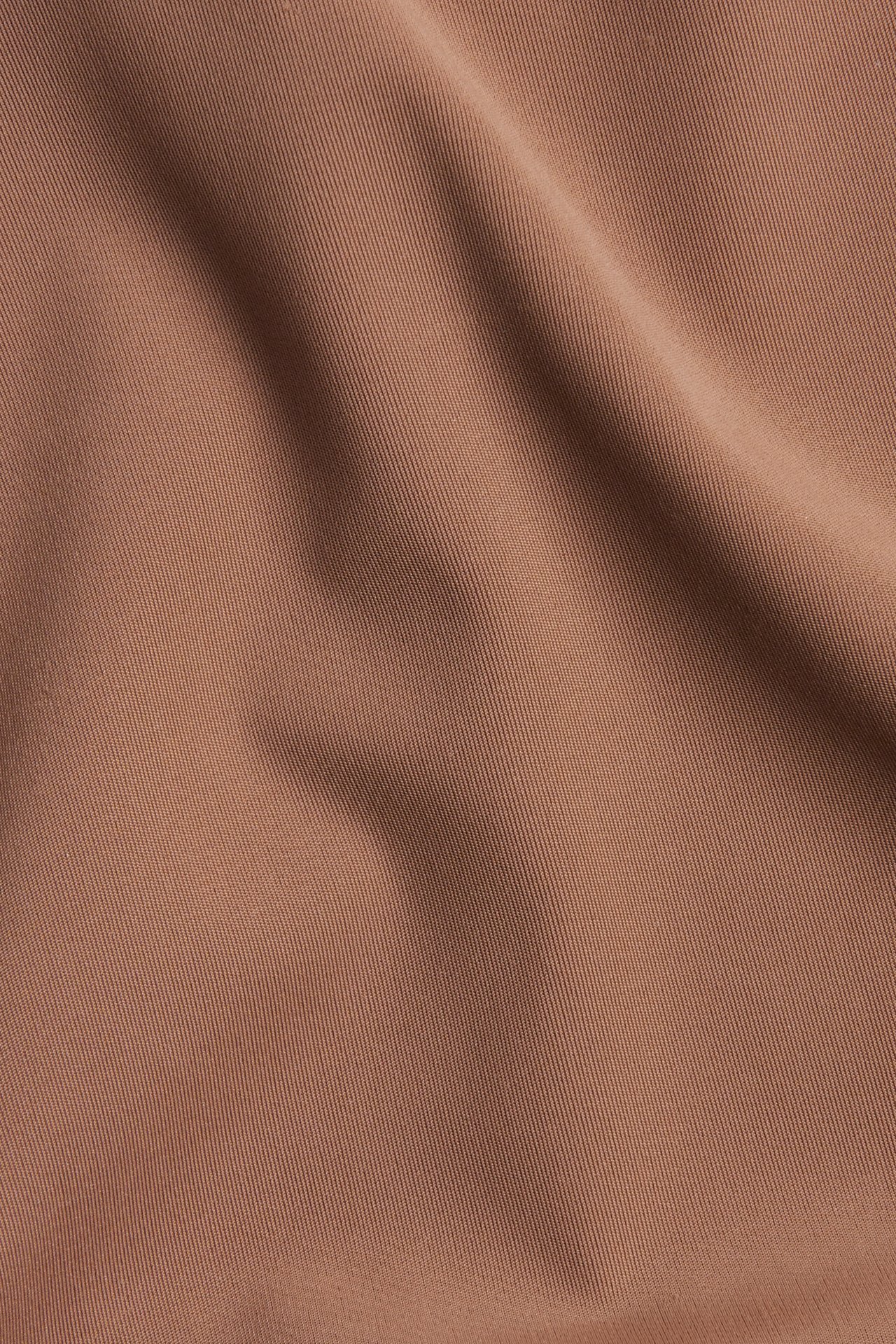 Lähikuva yksivärisestä ruskeasta mikrokuitukankaasta hienolla vinotekstuurilla ja kiillolla.