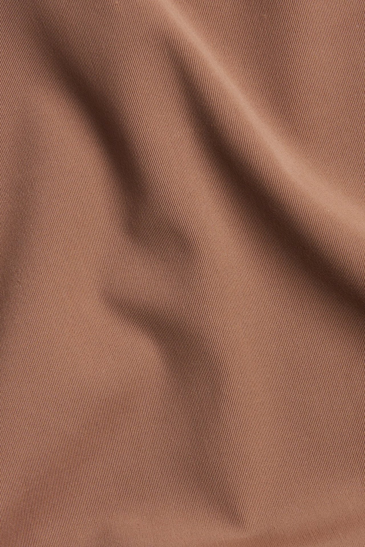 Lähikuva yksivärisestä ruskeasta mikrokuitukankaasta hienolla vinotekstuurilla ja kiillolla.