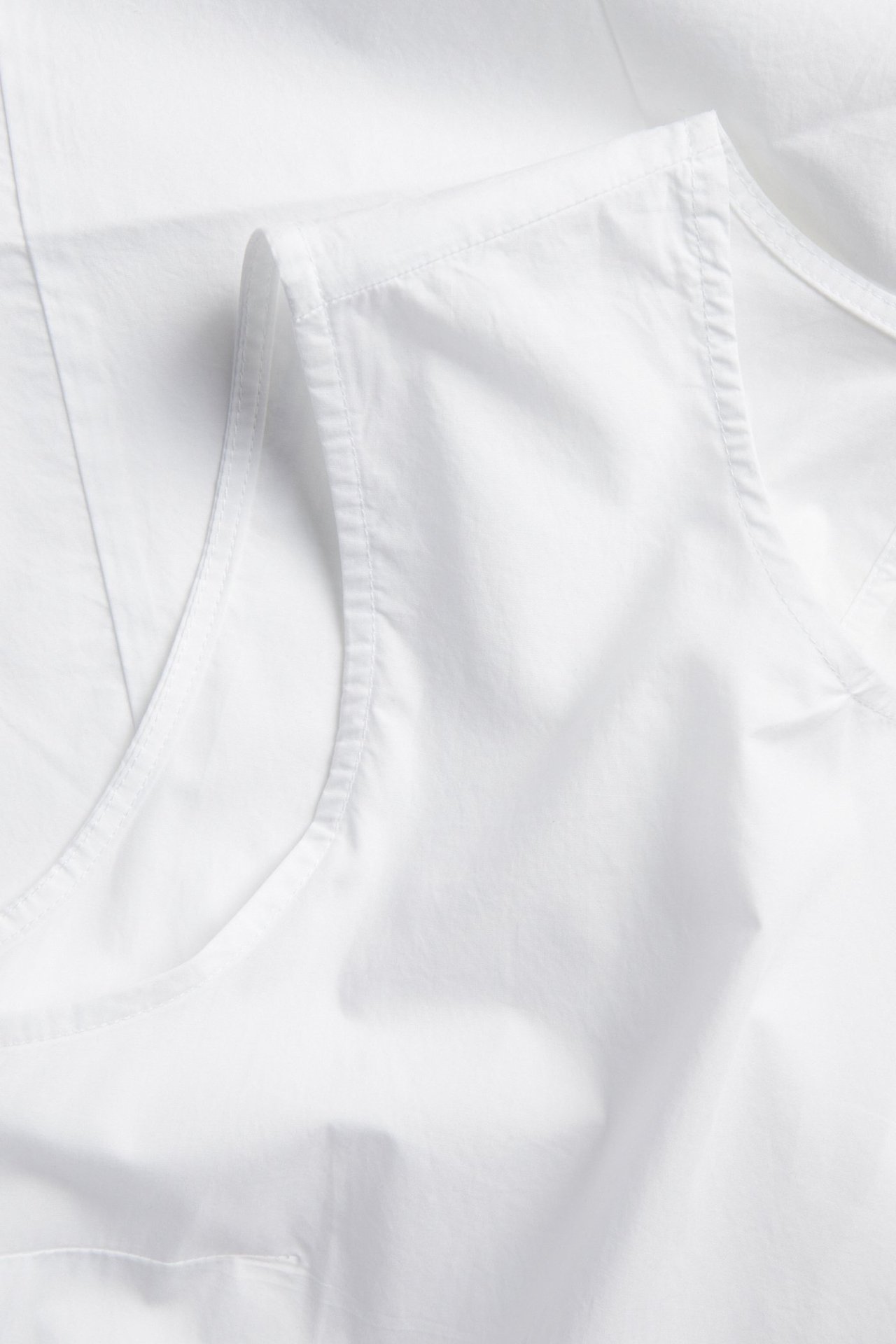 Lähikuva valkoisesta hihattomasta löysästi istuvasta puuvillamekosta, jossa näkyy pääntie ja kädentie.