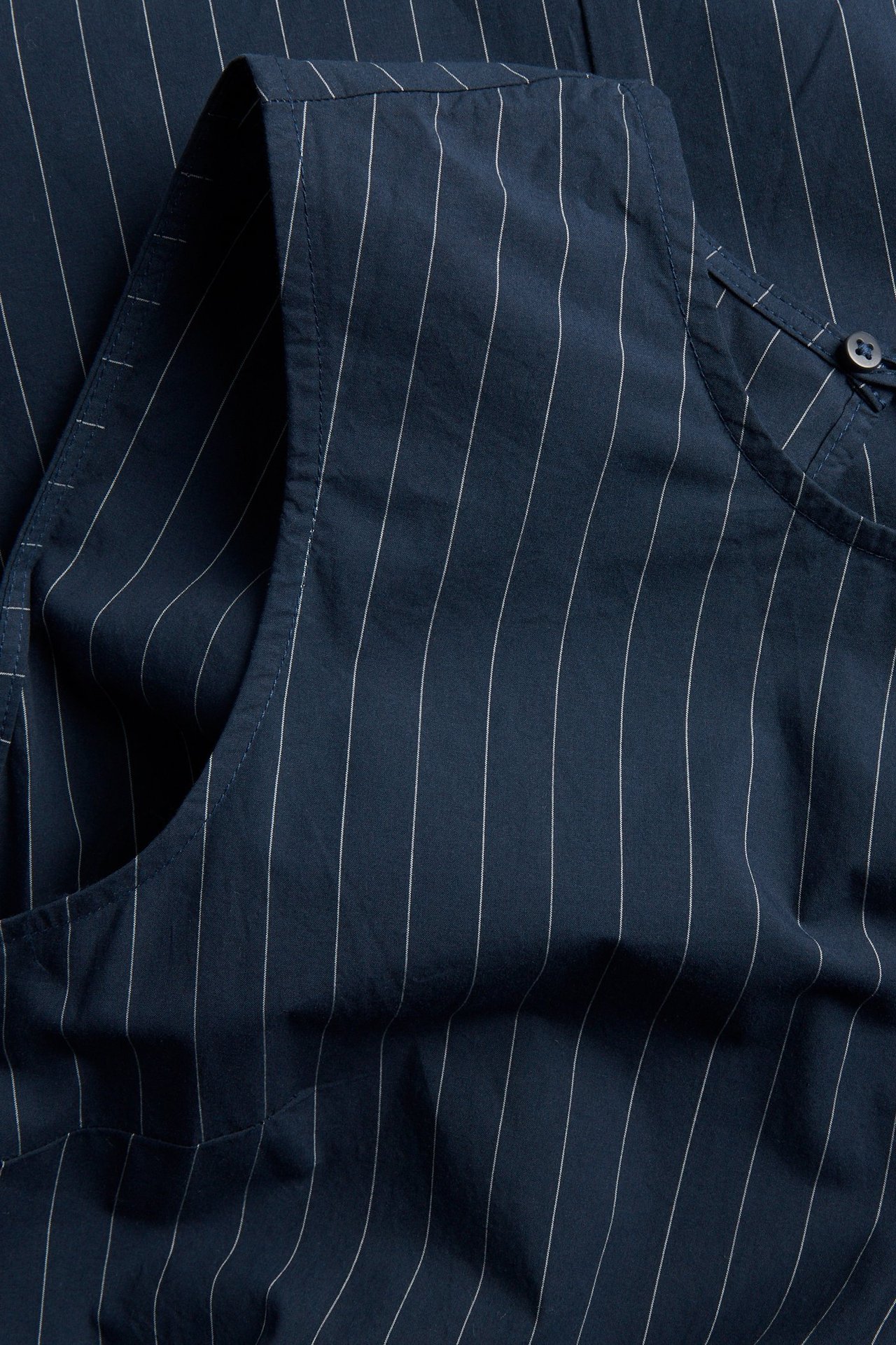 Lähikuva tummansinisestä, raidallisesta, hihattomasta puuvillamekosta pienellä nappiyksityiskohdalla.