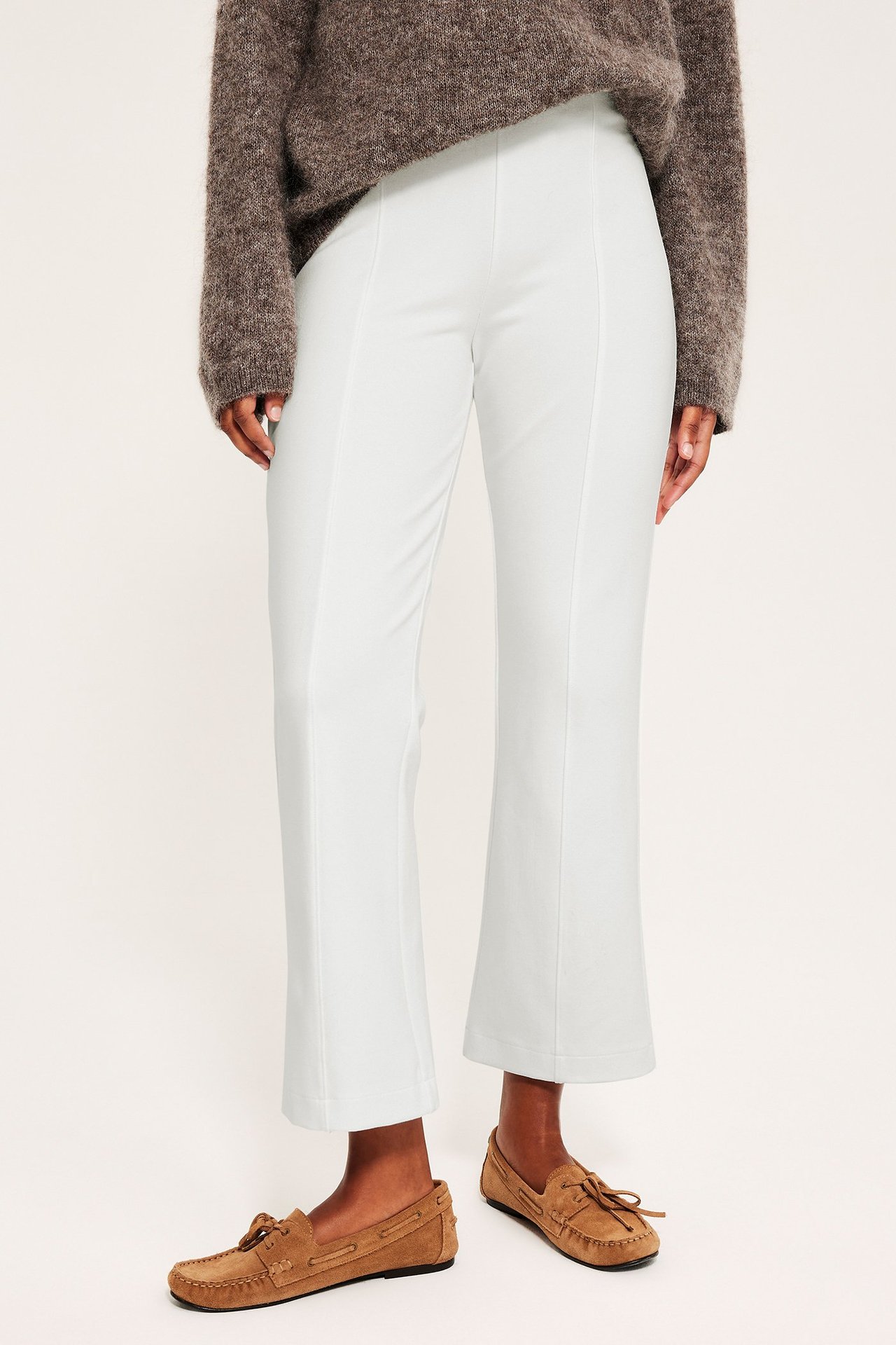 Nainen valkoisissa ommelasuissa, neule ja loafers, etunäkymä.