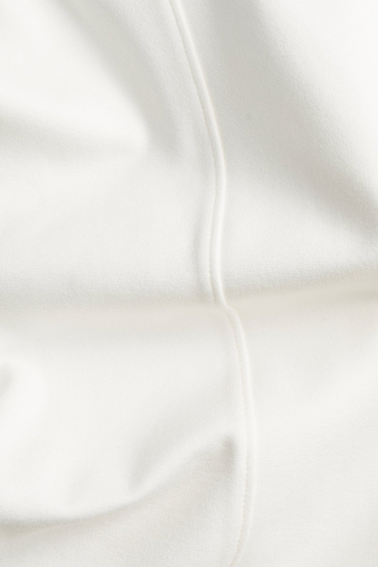 Zbliżenie na materiał spodni w kolorze ecru z widocznymi szwami z przodu.