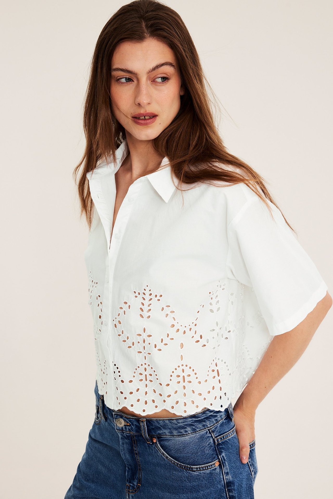 Edestäpäin, nainen valkoisessa lyhythihaisessa, lyhyessä puuvillapaidassa reikäbrodyyrillä ja sinisissä farkuissa.