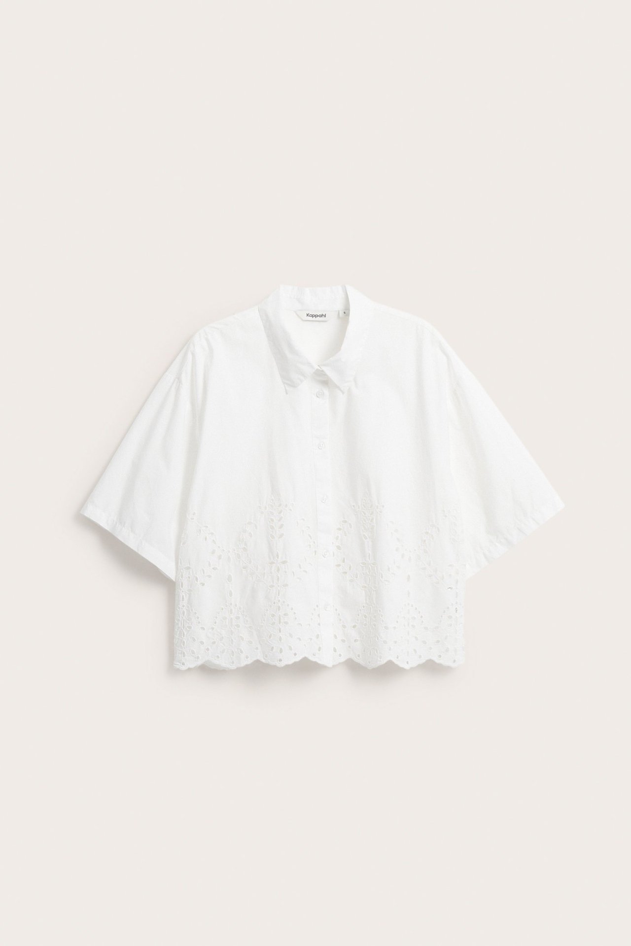 Edestä valkoinen puuvillainen lyhythihainen paita, broderie anglaise-kuvioinnilla ja aaltomaisella helmalla.