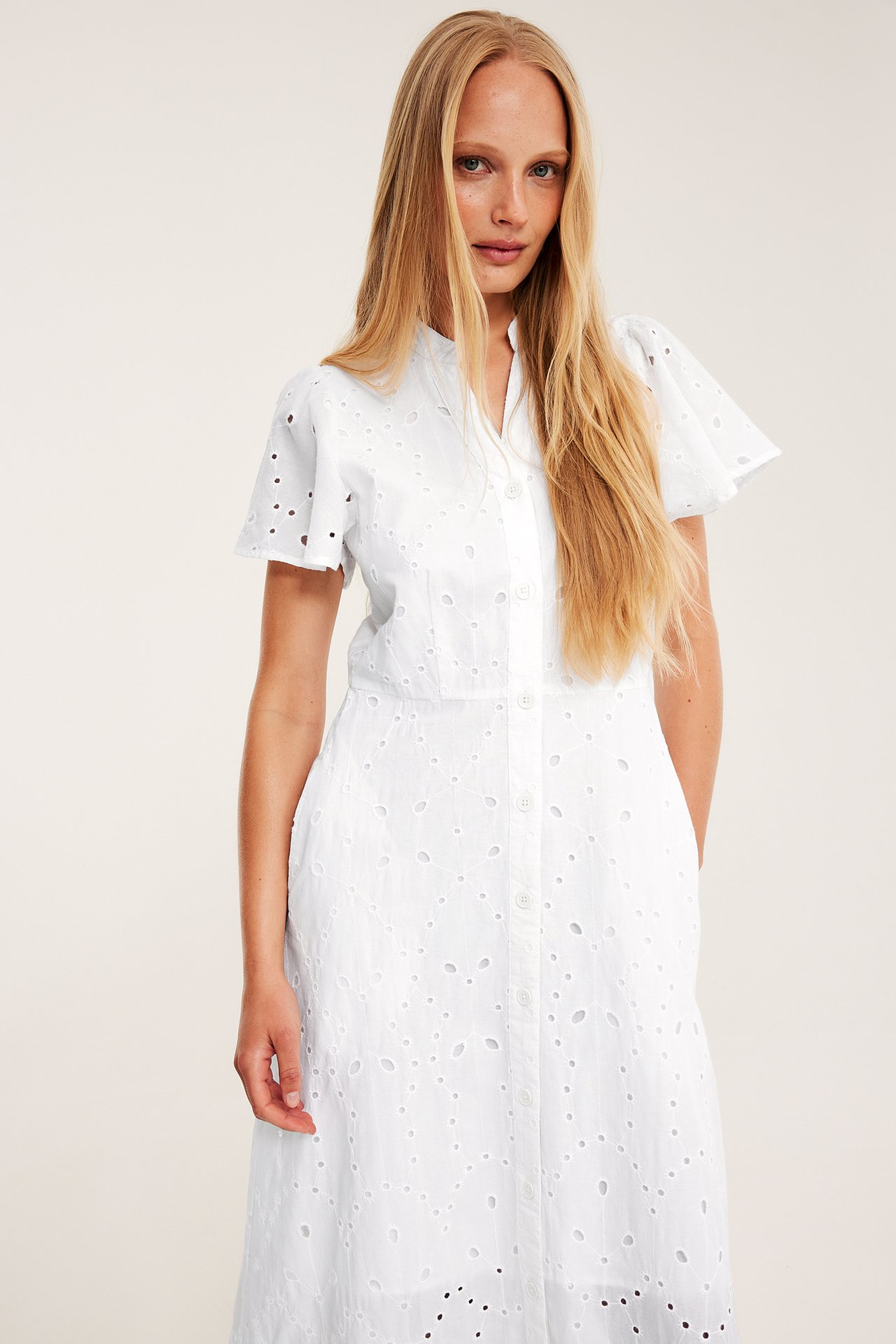 Framifrån: kvinna i vit bomullsklänning med broderie anglaise och korta volangärmar.
