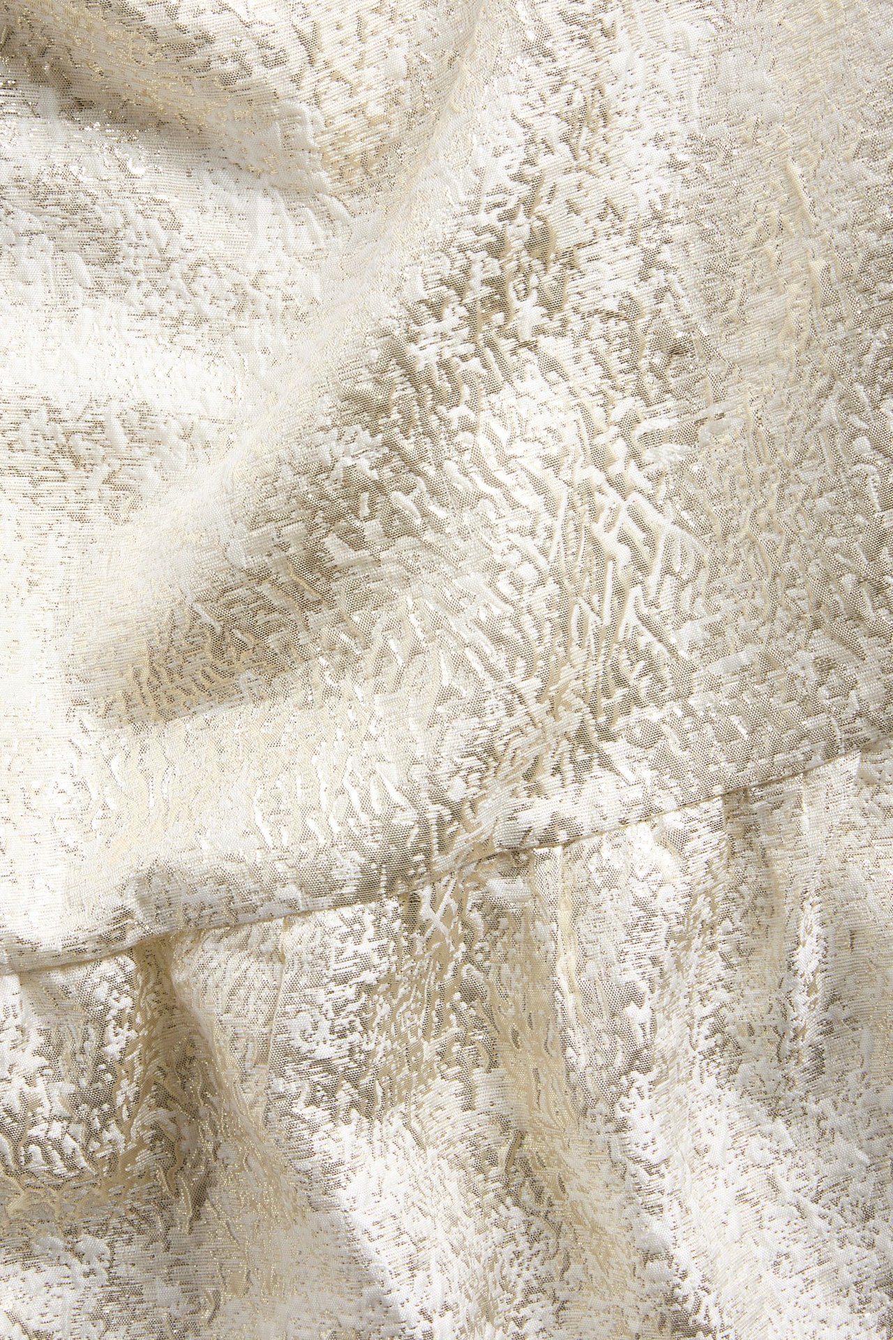 Närbild av offwhite och guldfärgat jacquardmönstrat klänningstyg med texturerad yta.
