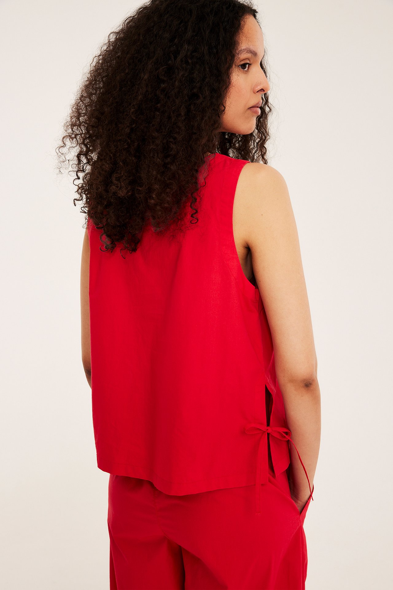 Widok z boku kobiety w czerwonym topie bez rękawów z wiązaniem i czerwonych spodniach.