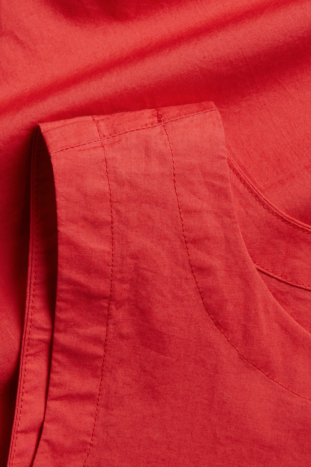 Lähikuva punaisesta puuvillakankaasta hihattomasta topista, näkyvät ompeleet taitetussa reunassa.