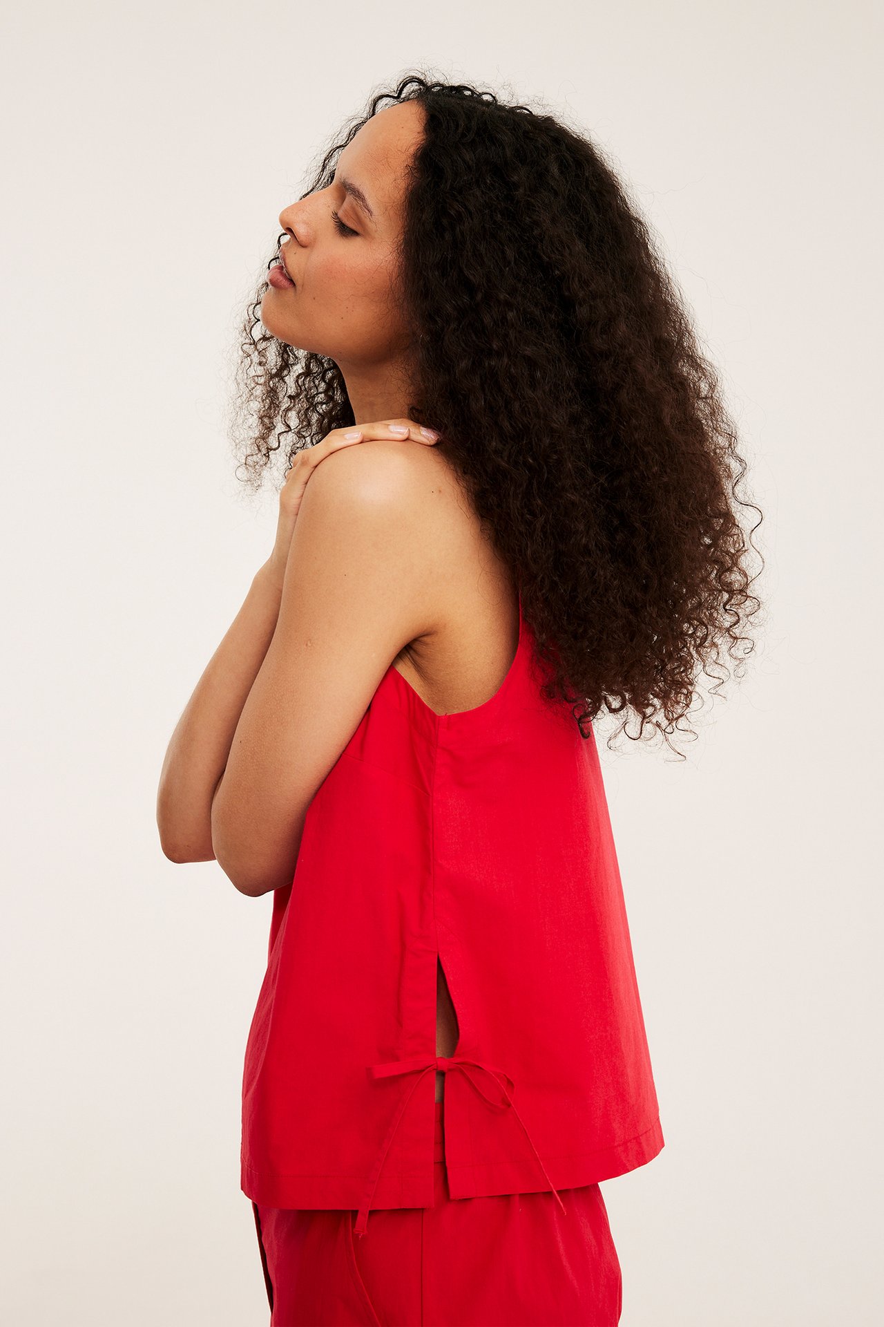 Naisen sivukuva, yllään punainen hihaton toppi, jossa on sivuhalkiot ja solmiot, punaisilla shortseilla.
