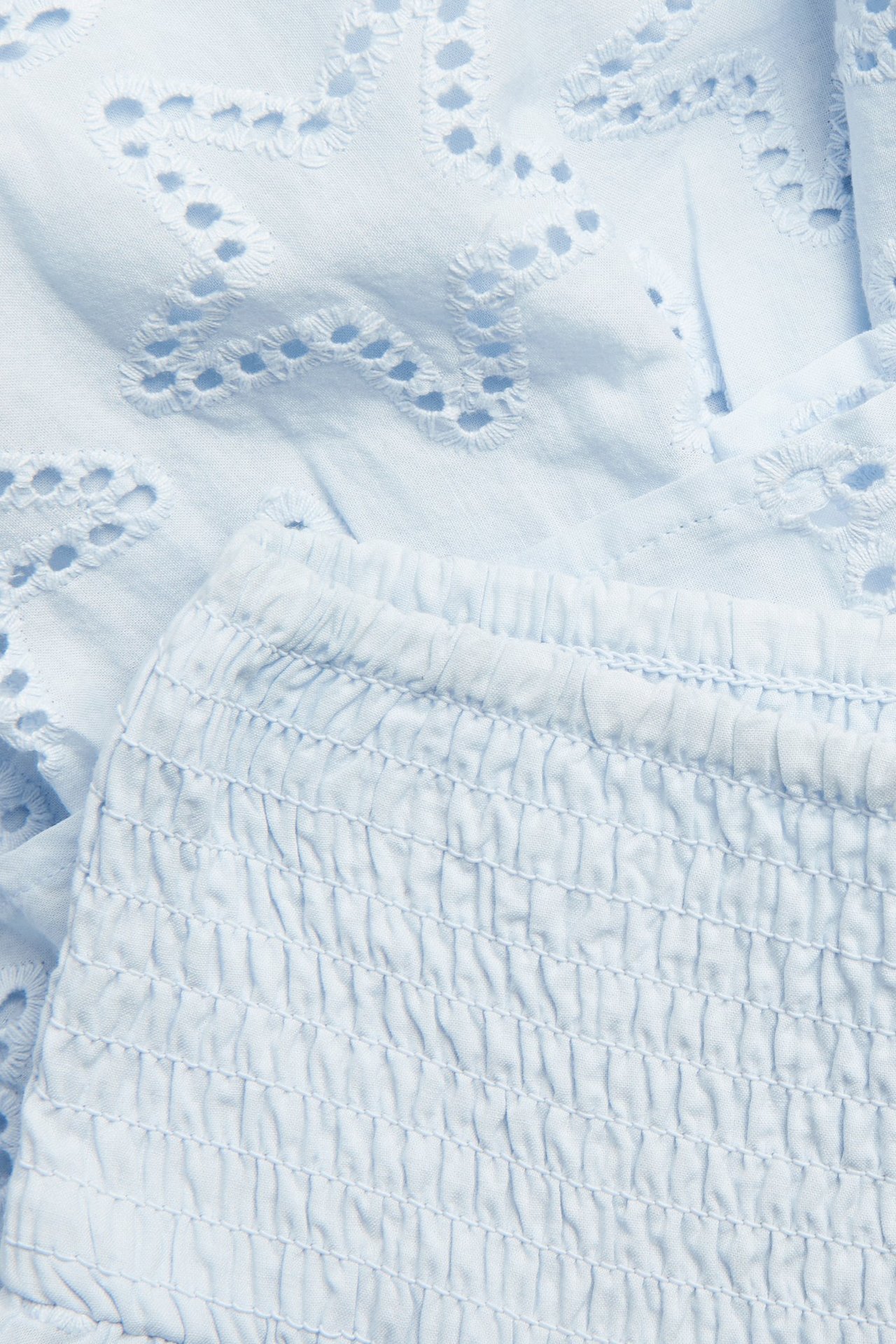 Närbild av en ljusblå volangkjol i bomull med stjärnmönstrad broderie anglaise och smockad midja.