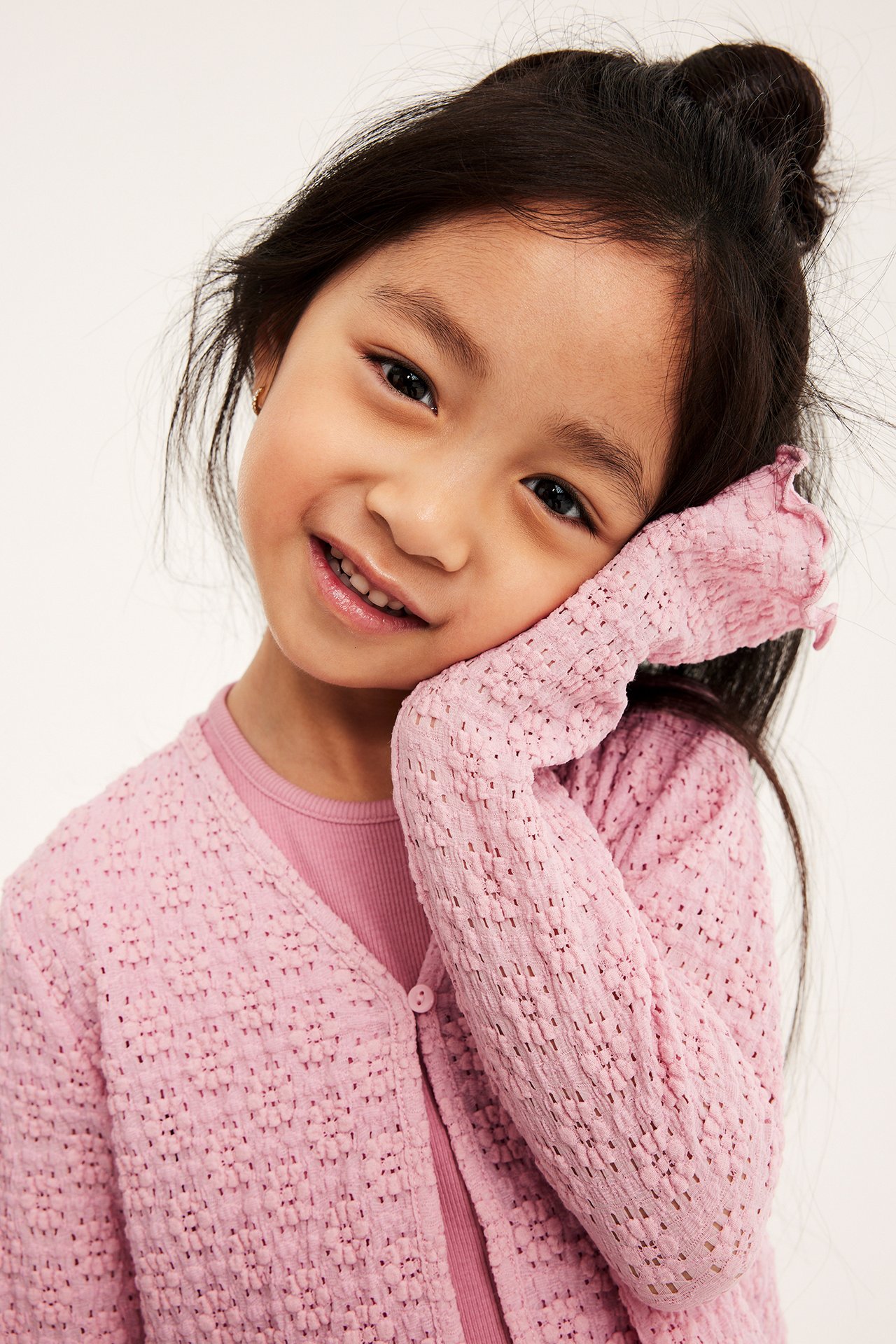 Nära frontvy av ett barn i ljusrosa spetskofta i jersey med en knapp över en rosa topp.