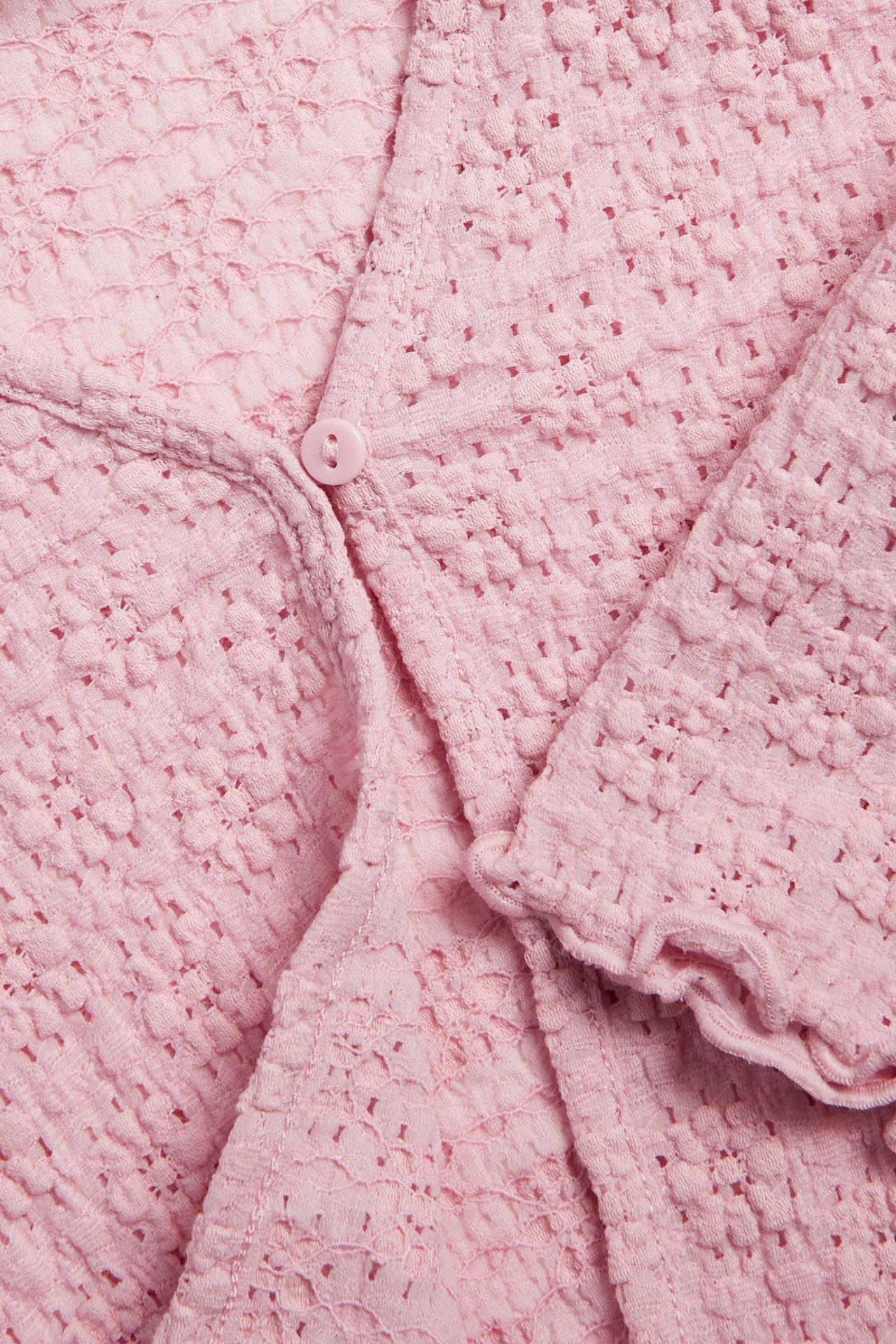 Zbliżenie na jasnoróżowy koronkowy kardigan z jednym guzikiem i falbankowym mankietem.