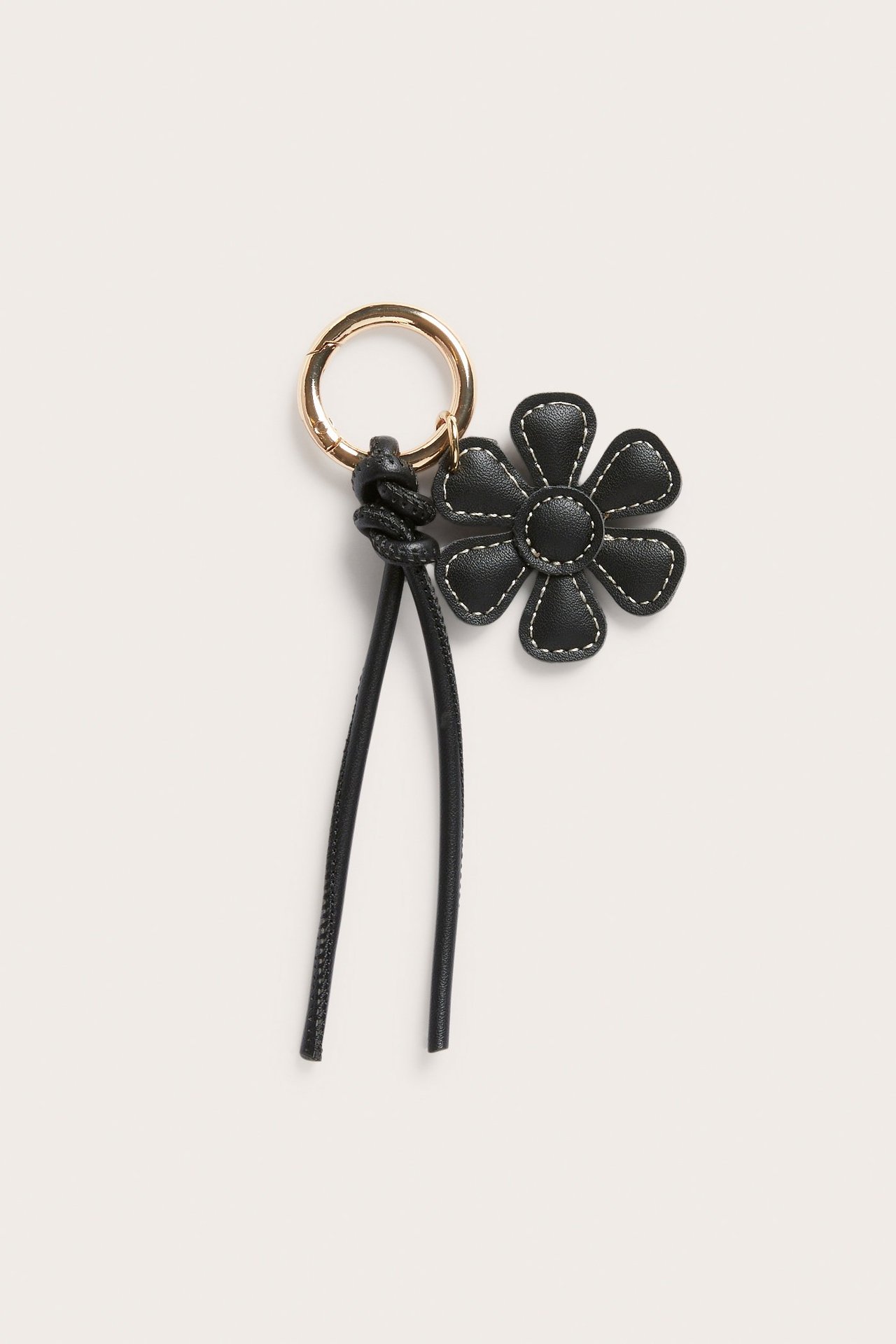 Nærbilde av en svart nøkkelring i imitert skinn, blomsterformet med hvit søm og gullfarget metallring.