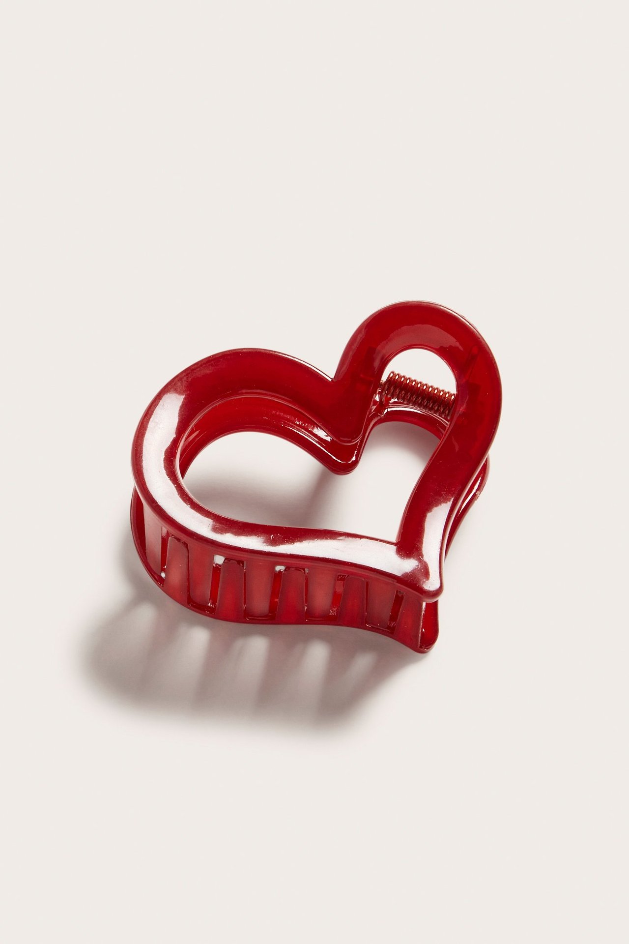 Lähikuva vinosta kulmasta kiiltävästä, läpikuultavasta punaisesta sydämenmuotoisesta hiusklipsistä näkyvällä metallijousella.