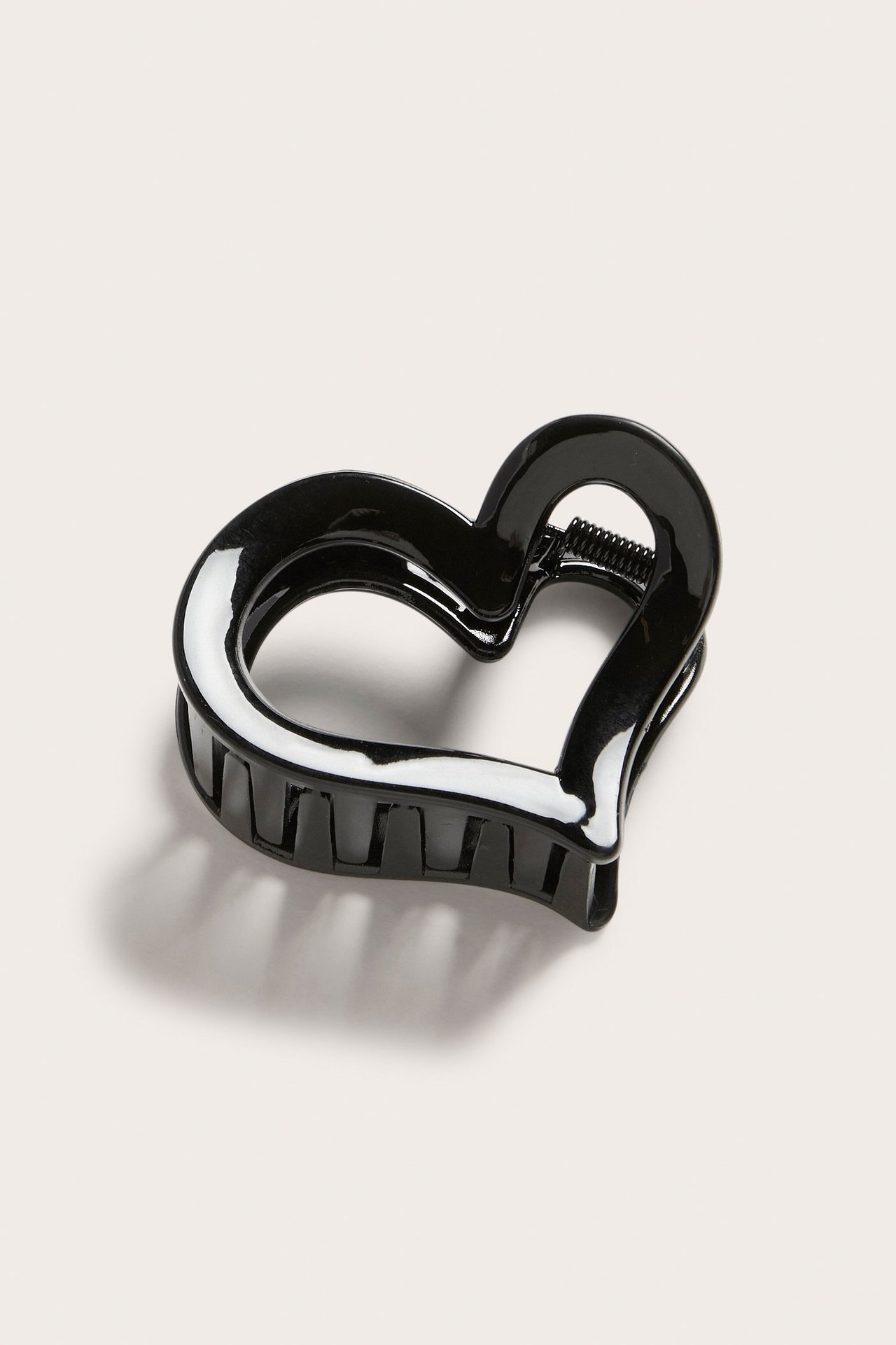 Lähikuva kiiltävästä mustasta sydämenmuotoisesta hiusklipsistä näkyvällä jousella.