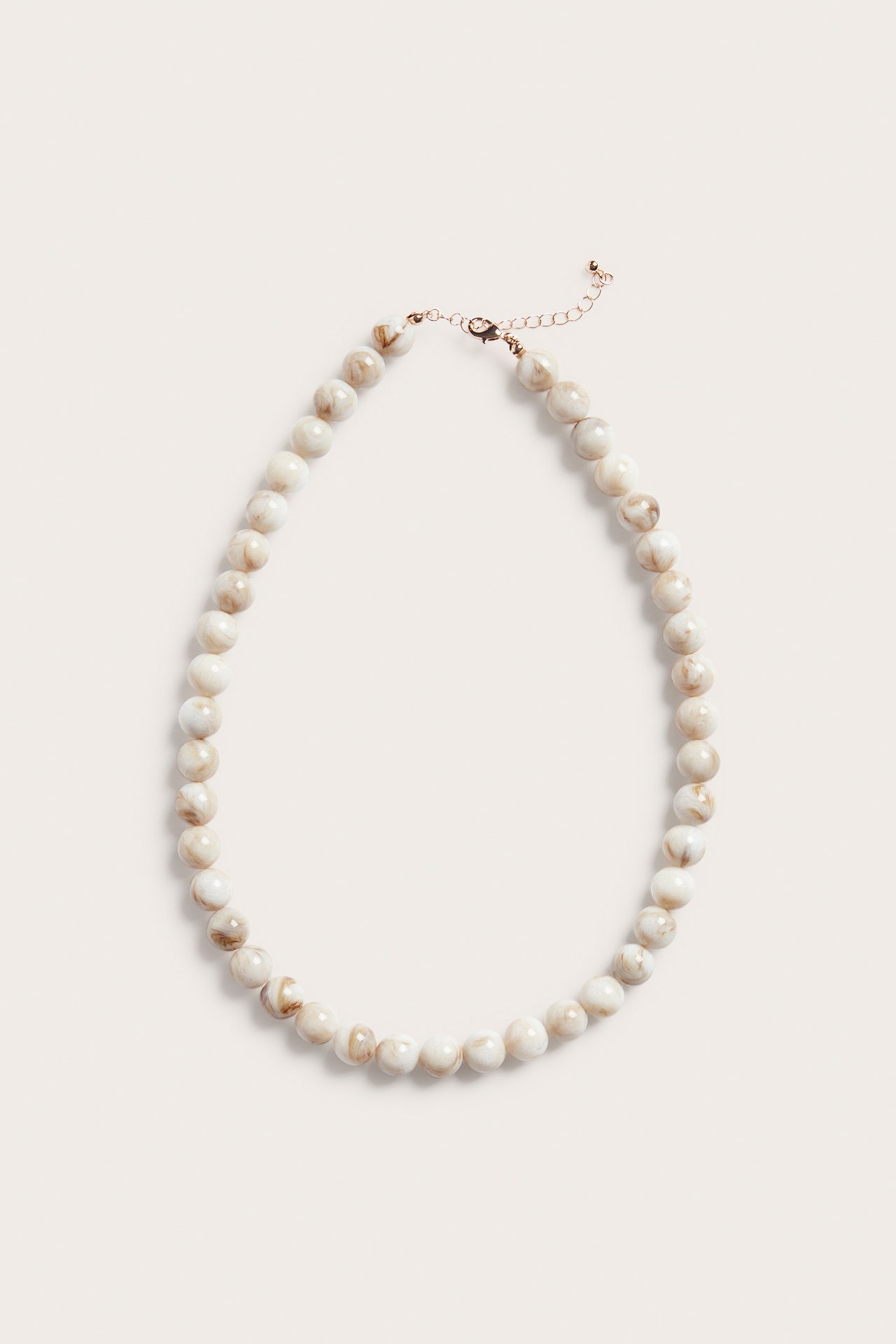 Ovanifrån: ett ljusbeige marmorerat pärlhalsband i plast med guldfärgat klospänne och förlängningskedja.