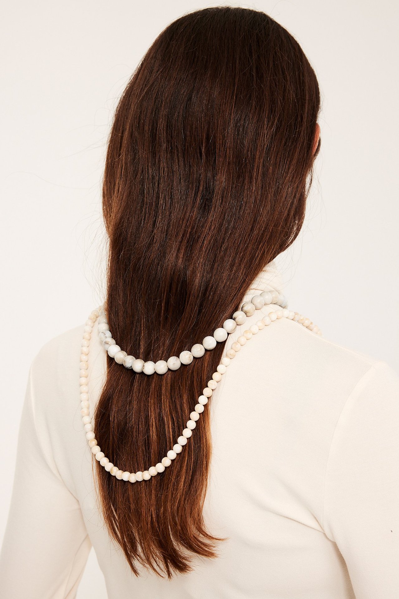 Bakfra av kvinne med langt lys beige plastperlekjede over brunt hår.