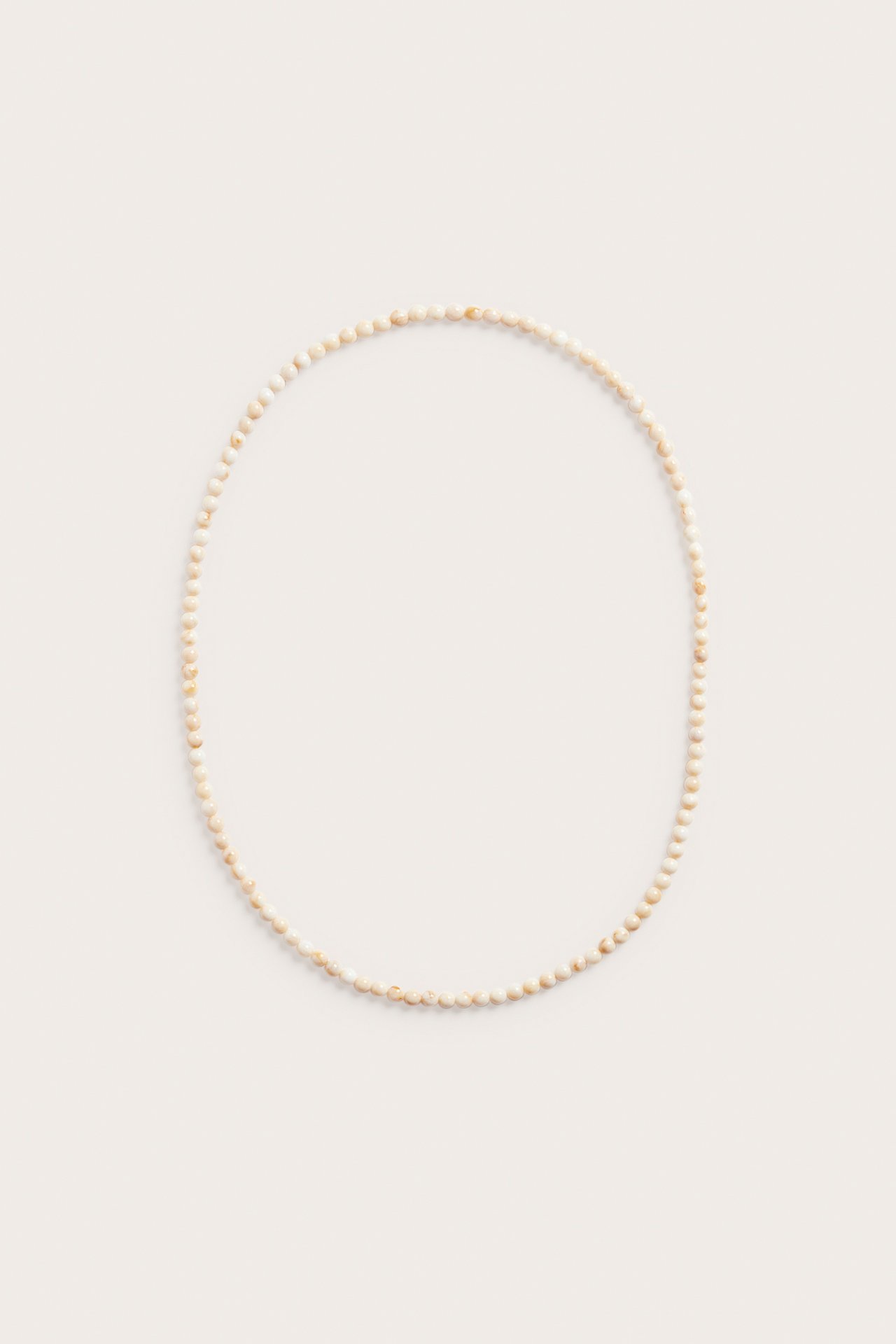 Toppvy av ett långt halsband med små, ljusbeige plastpärlor, arrangerat i en cirkel.
