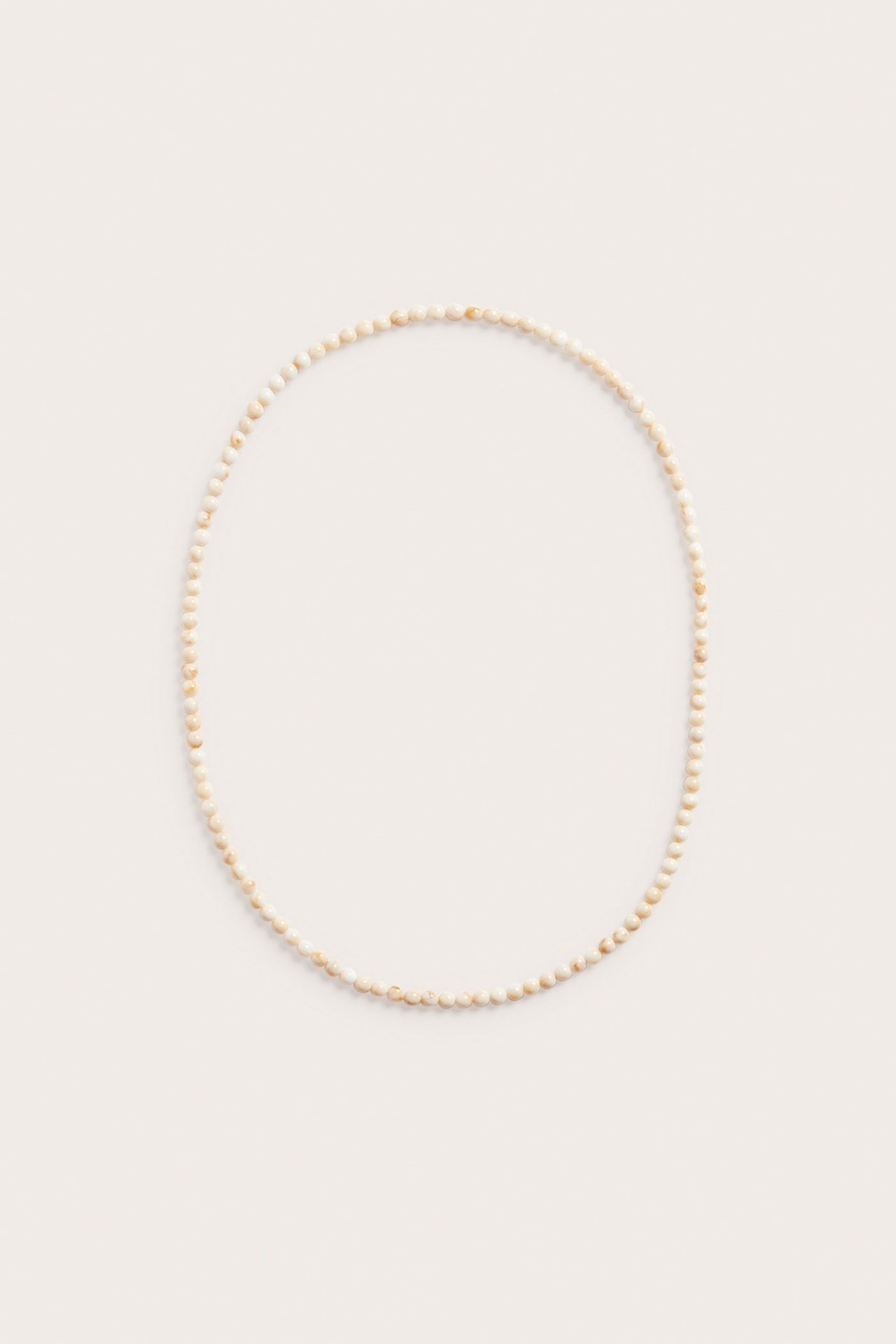 Toppvisning av et langt kjede med små, lysebeige plastperler, ordnet i en sirkel.