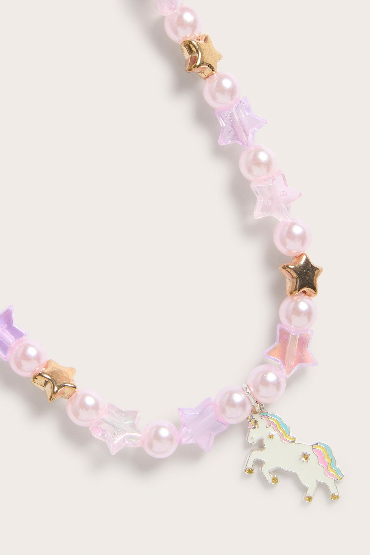 Zbliżenie na jasnoróżowy naszyjnik z koralików, z opalizującymi i złotymi gwiazdkami oraz jednorożcem.