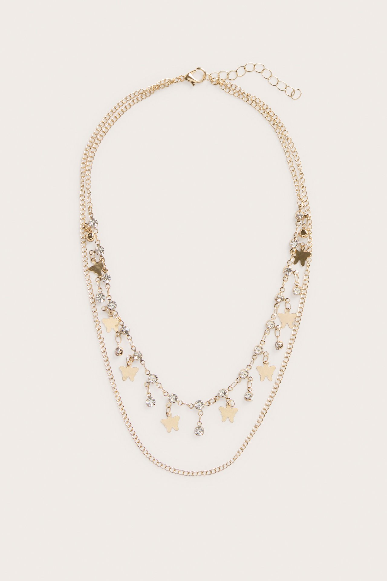 Edestäpäin, kaksirivinen kultainen kaulakoru, jossa perhoskoristeita, kirkkaita strasseja ja papukaijalukko.