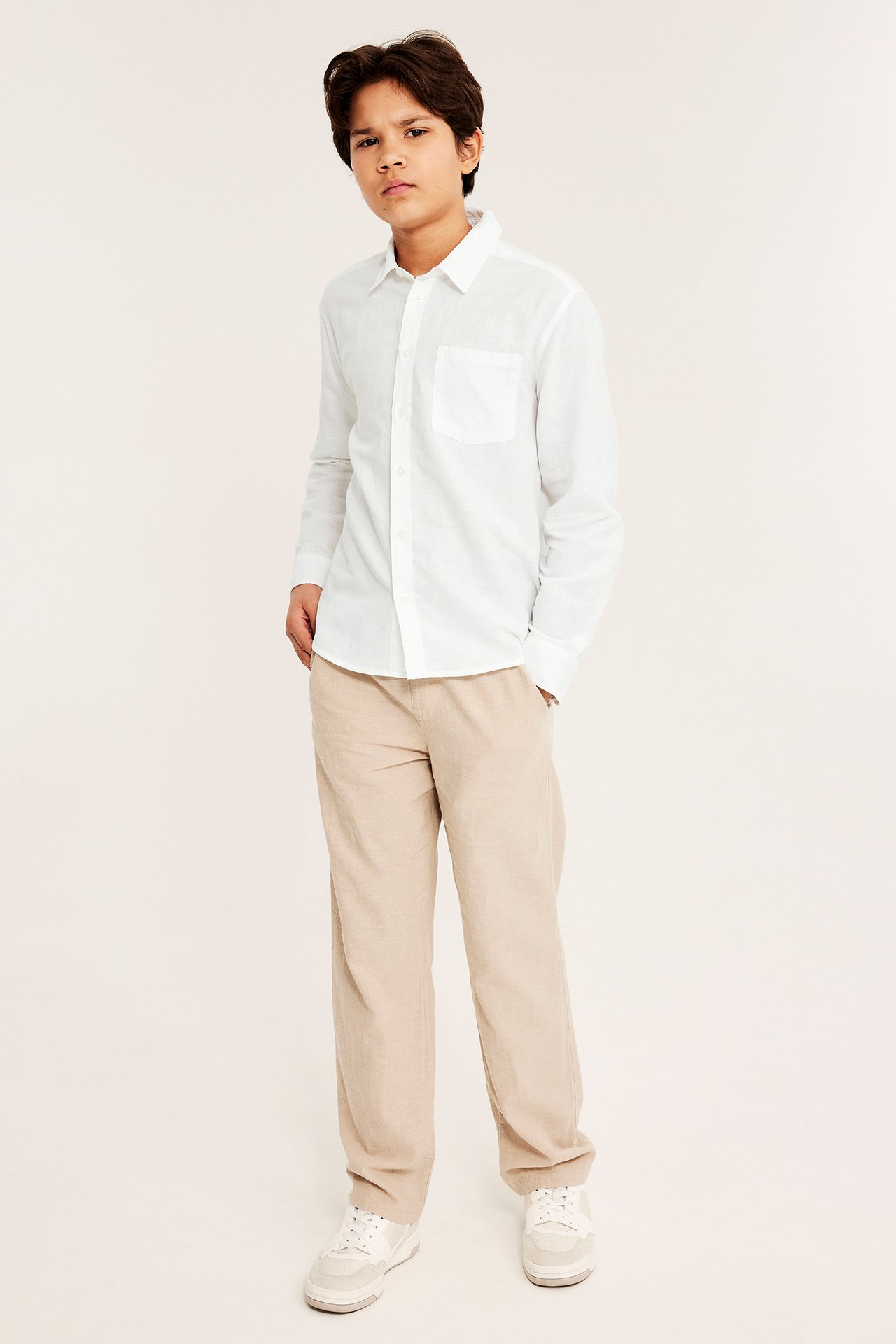 Frontbilde av et barn i hvit linblanding-skjorte, beige bukser og hvite joggesko.