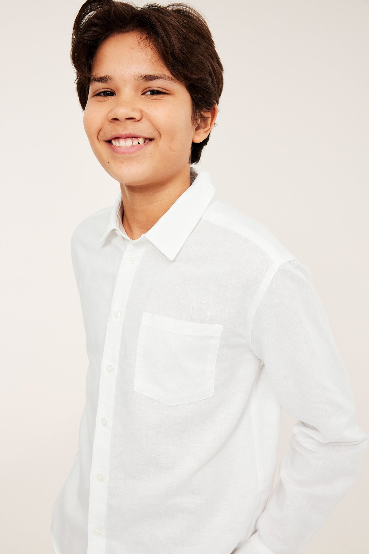 Framifrån: Leende barn i vit linneblandningsskjorta med bröstficka och knäppning framtill.