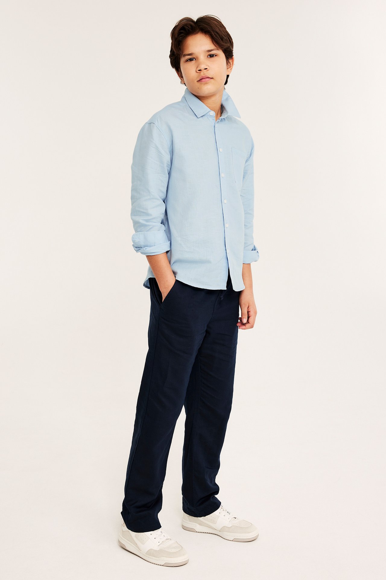 Frontbilde av et barn iført en lyseblå linskjorte, mørkeblå bukser og lyse joggesko.