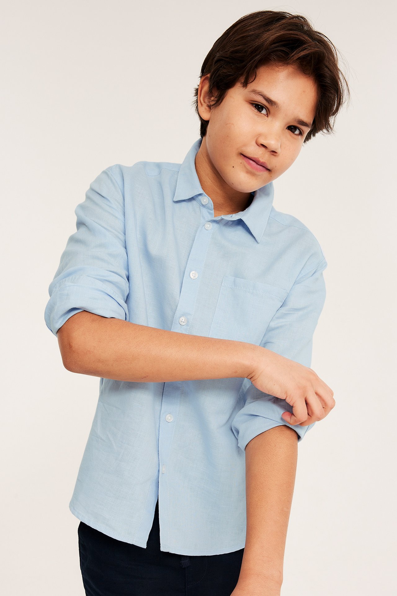 Frontbilde av et barn i lyseblå linskjorte, med oppbrettede ermer og mørke bukser.