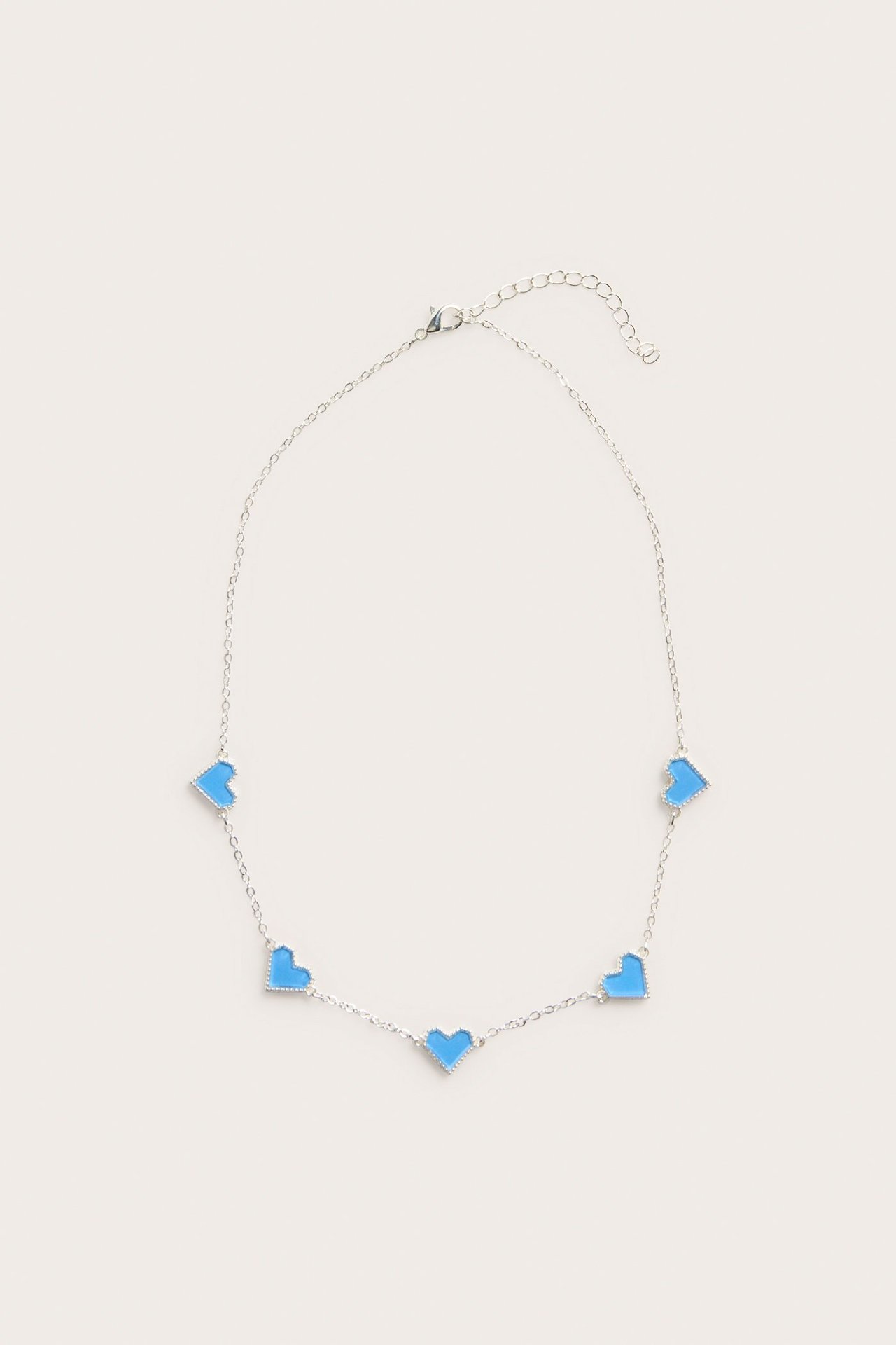 Lähikuva, edestä, hopeanvärisestä metallikaulakorusta, jossa on viisi sinistä sydänriipusta ja papukaijalukko.