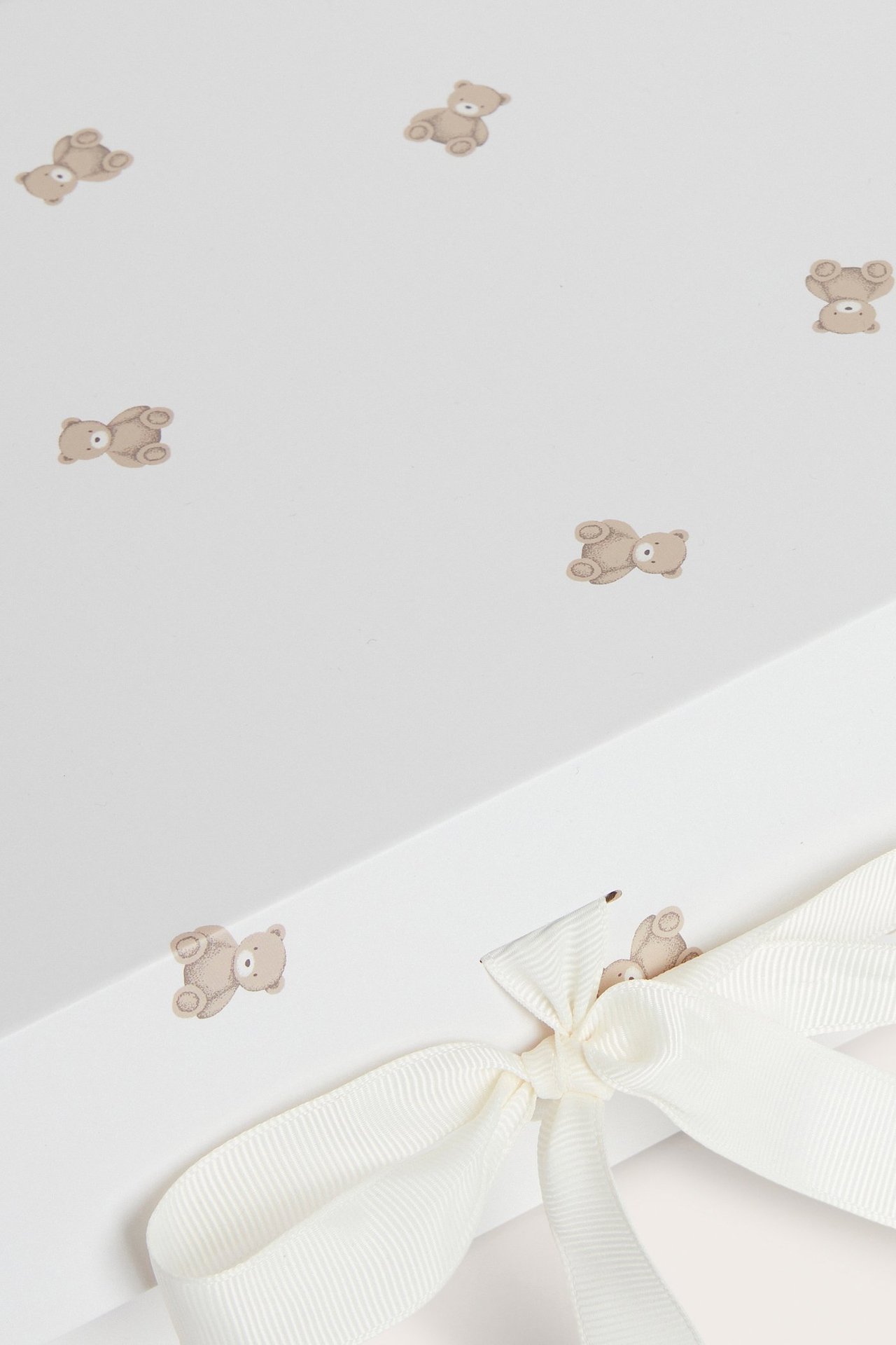 Nära bild av en offwhite presentlåda i papper med brun björnprint och ett beige band knutet som rosett.