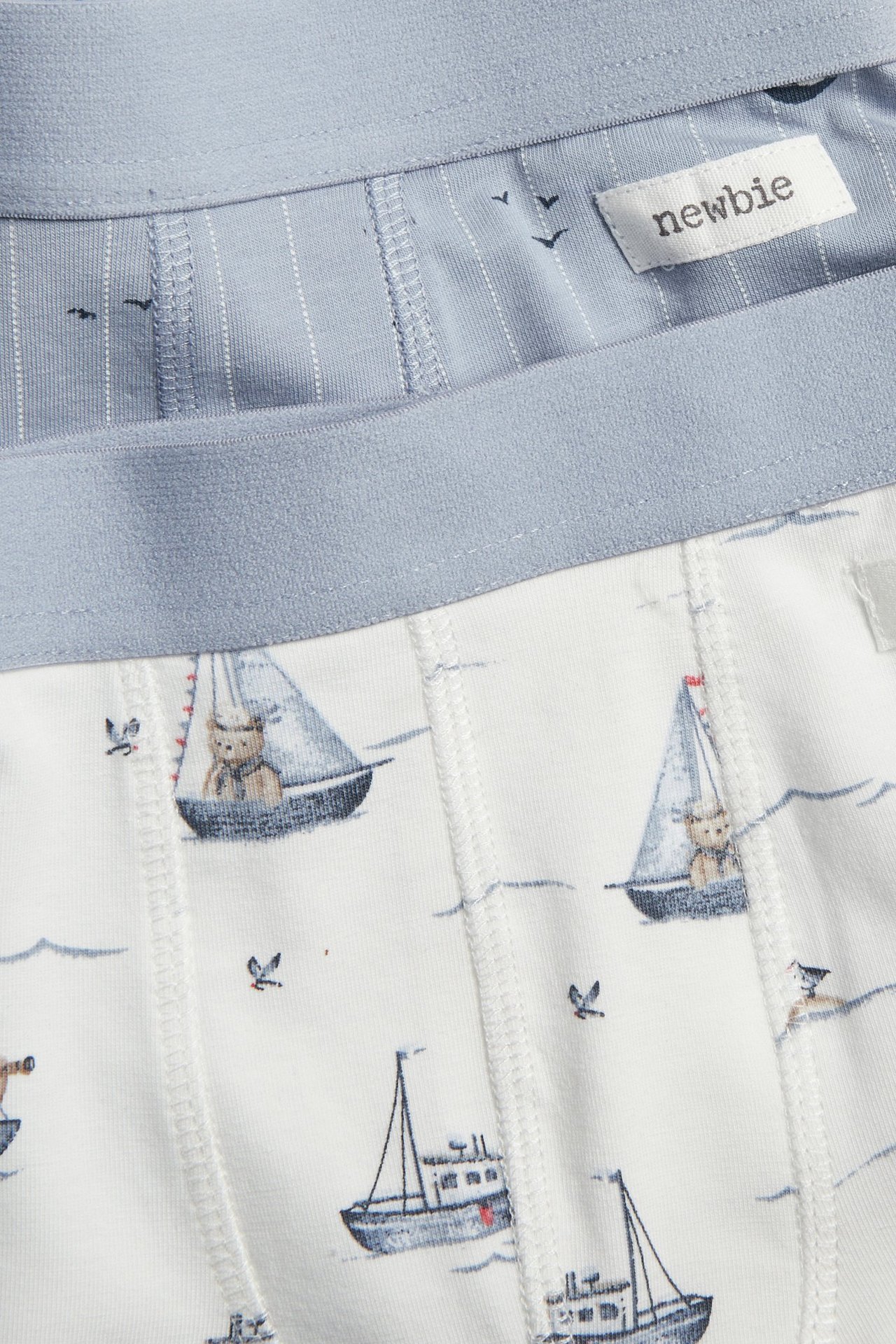 Zbliżenie na dwupak bokserek dziecięcych: jedne białe z żaglówkami, drugie niebieskie w paski.