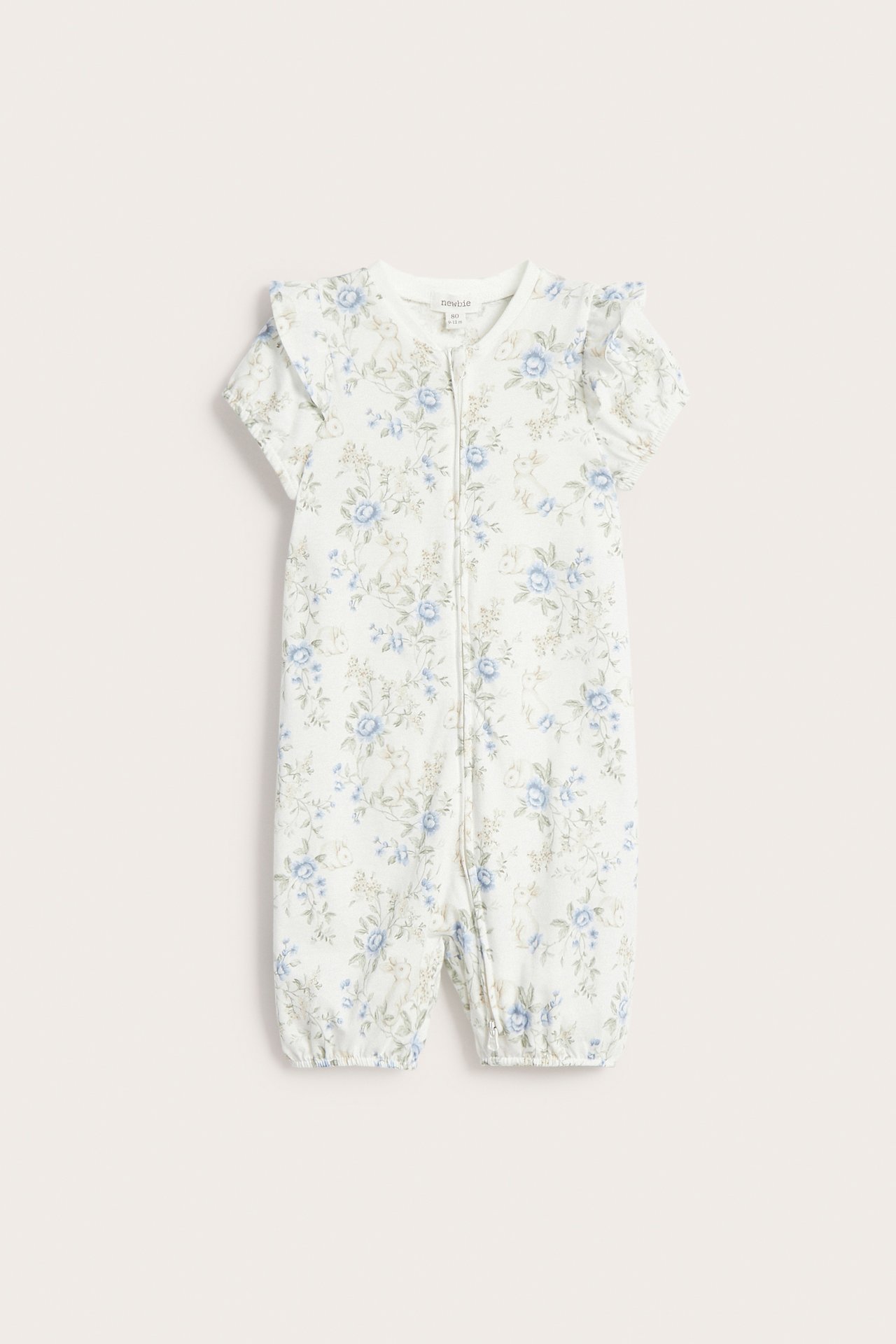 Edestä luonnonvalkoinen vauvan lyhythihainen pyjama, kukkakuvio, röyhelöt, painonapit.