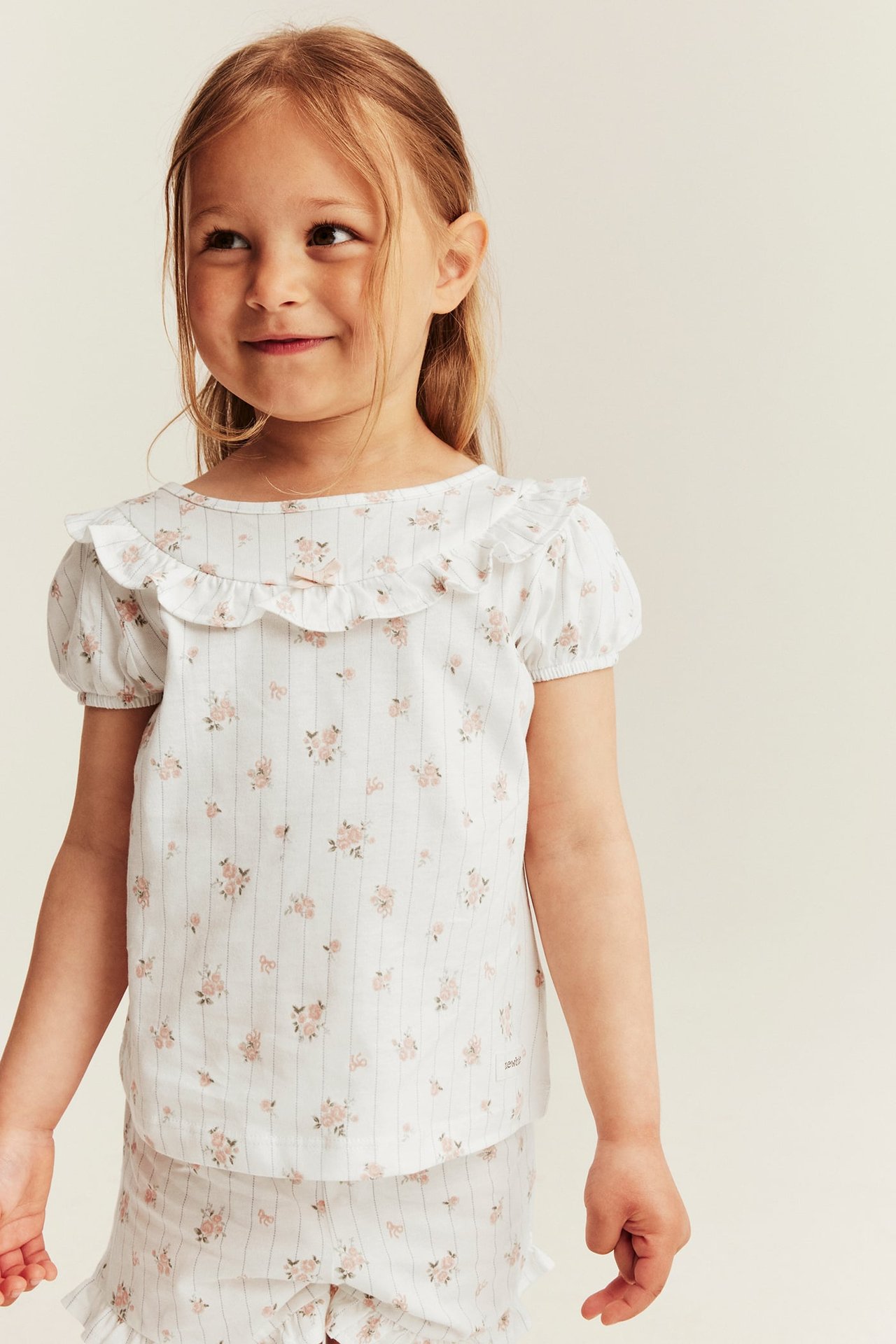 Frontbilde av et barn i offwhite blomstret og stripet bomullspyjamas-topp med rysjer og matchende shorts.