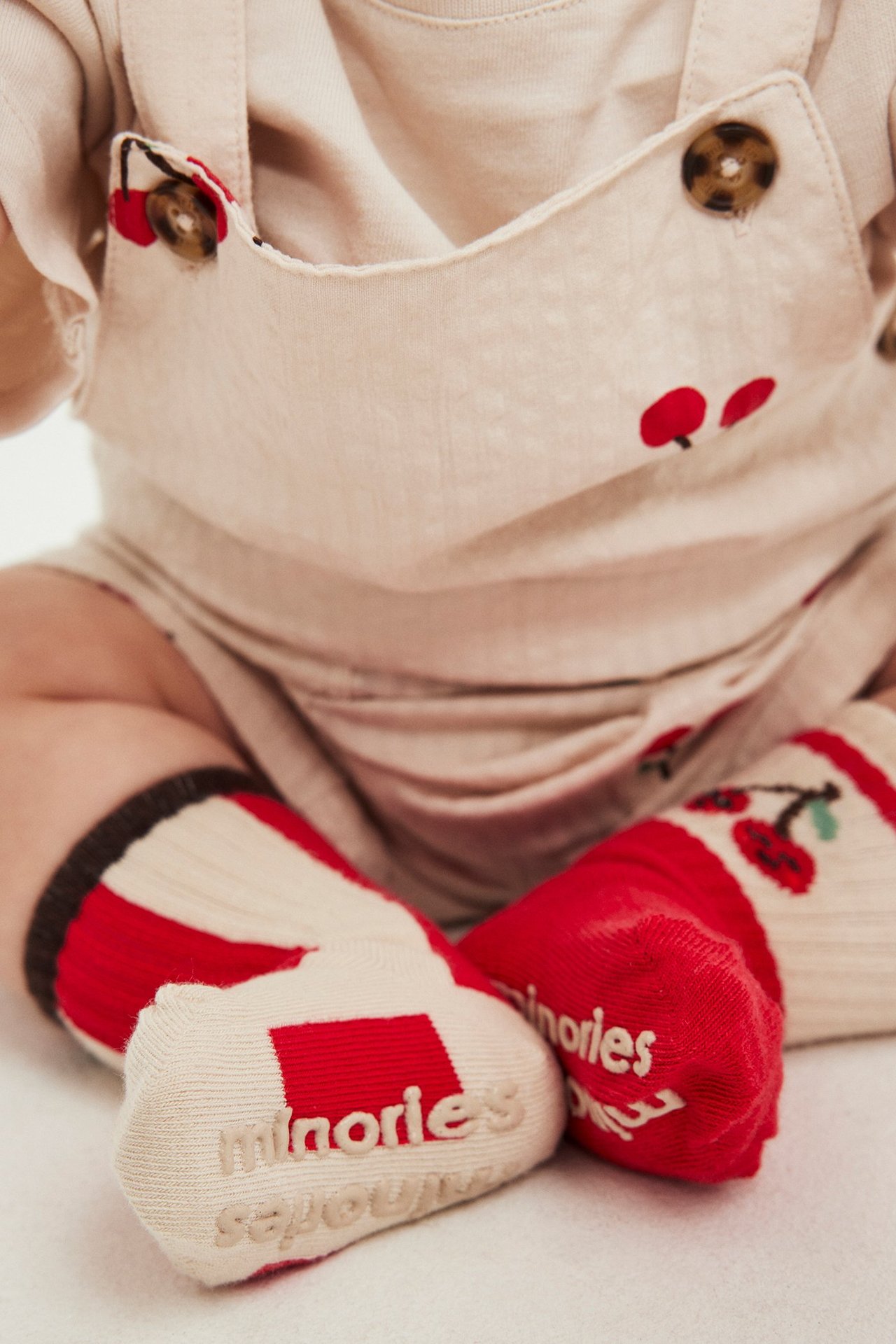 Närbild på baby i röda och vitmönstrade strumpor med halkskydd och en beige körsbärsmönstrad sparkdräkt.