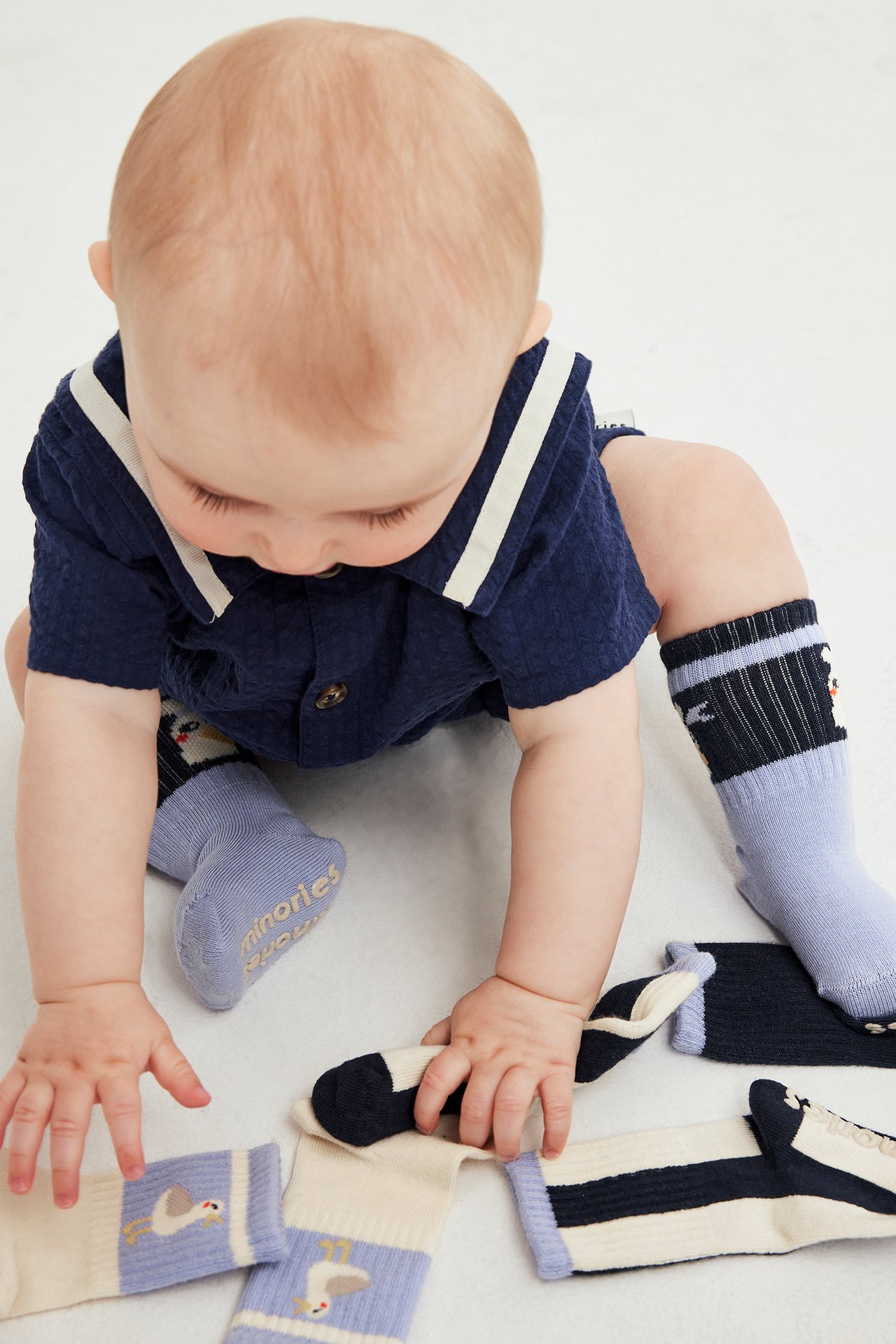 Widok z góry na dziecko bawiące się wzorzystymi skarpetkami; dziecko nosi niebieskie skarpety i granatowy top.