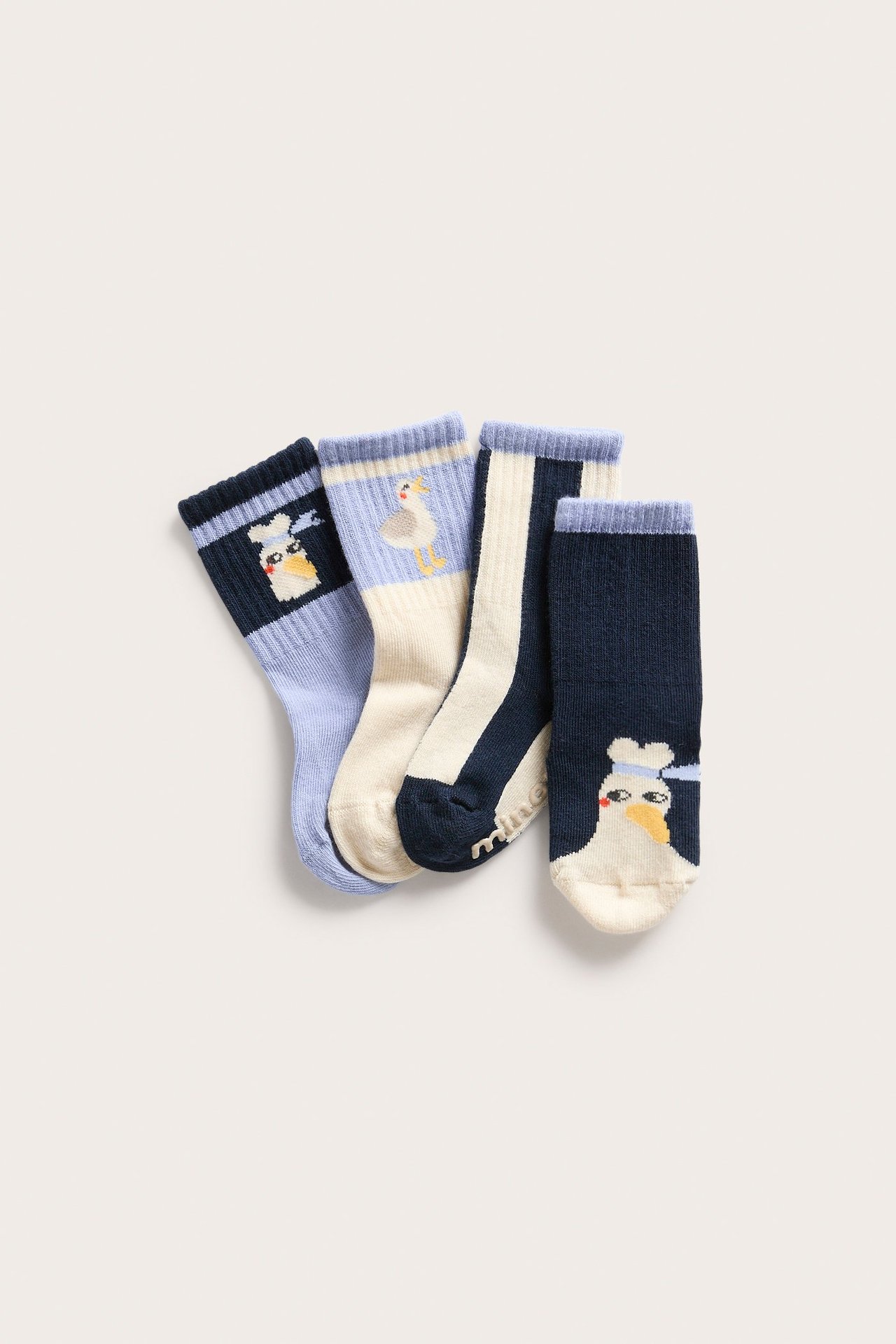 Widok z góry na czteropak skarpetek niemowlęcych: niebieskie, kremowe, paski i wzory zwierzęce z mewami.