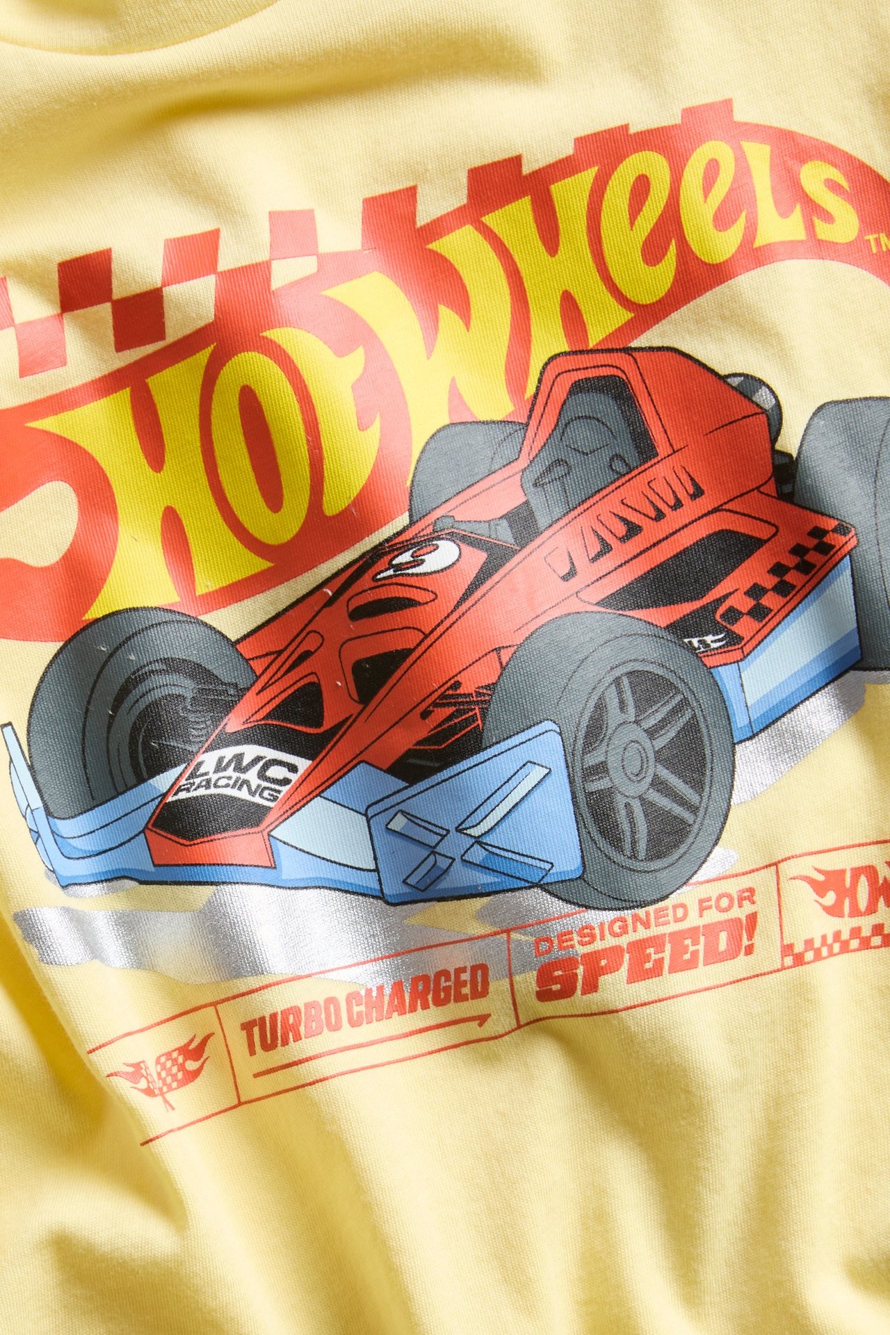 Lähikuva keltaisesta puuvillaisesta t-paidasta, jossa on värikäs Hot Wheels -kilpa-autopainatus.