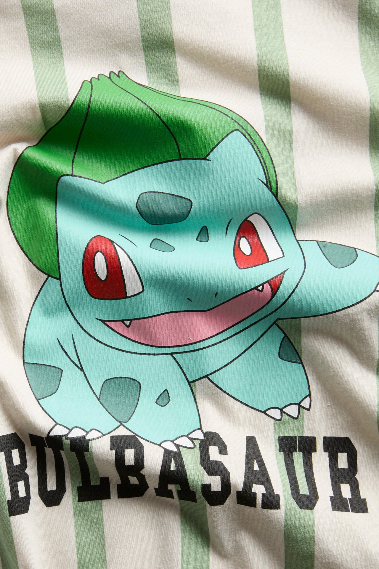 Närbild, framifrån, av en oversized beige randig bomulls-t-shirt med Bulbasaur Pokémon-tryck.