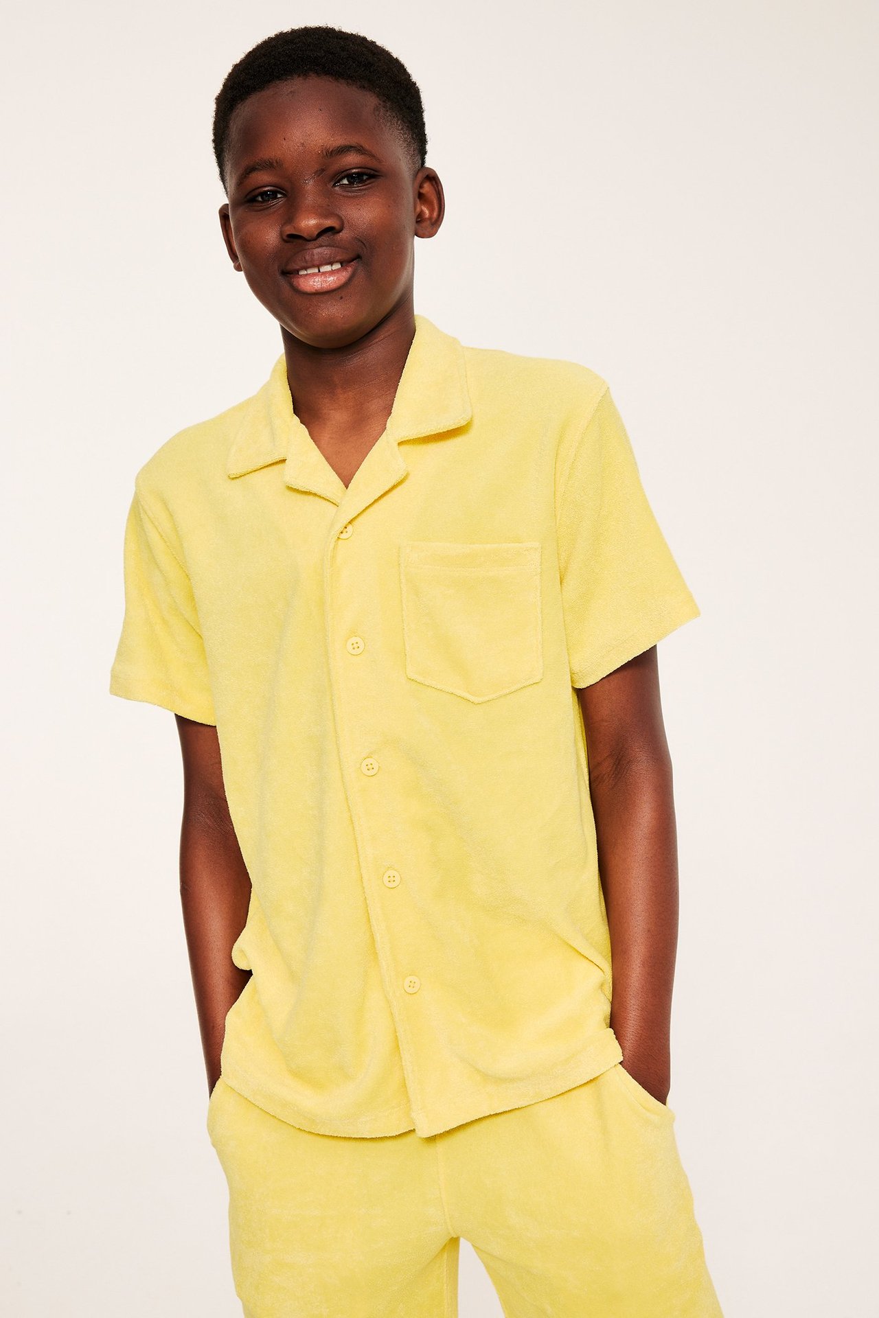 Frontvy av ett barn i gul kortärmad frottéskjorta med resortkrage, bröstficka och matchande shorts.
