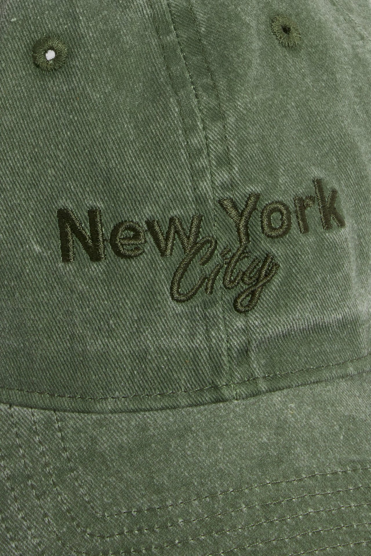 Zbliżenie na zieloną czapkę twillową z efektem sprania i haftem "New York City" z przodu.