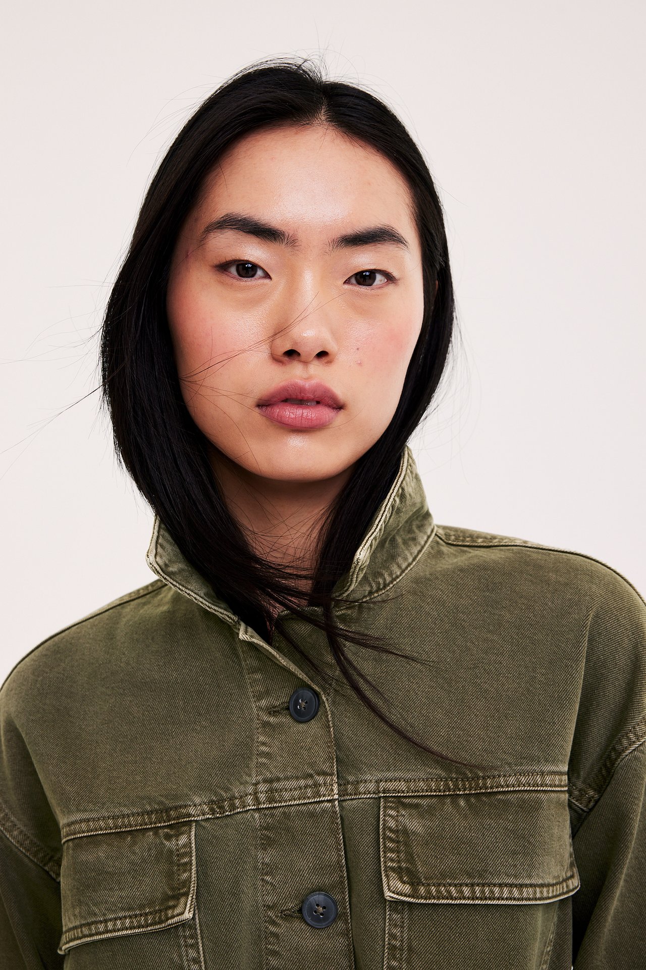 Lähikuva edestä naisesta vihreässä twill-utilitytakissa, jossa on paikkataskut ja napit.