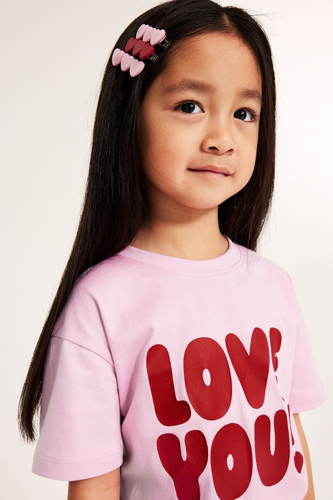 Zbliżenie z przodu: dziecko nosi trzy serduszkowe spinki do włosów, dwie jasnoróżowe, jedną ciemnoróżową.