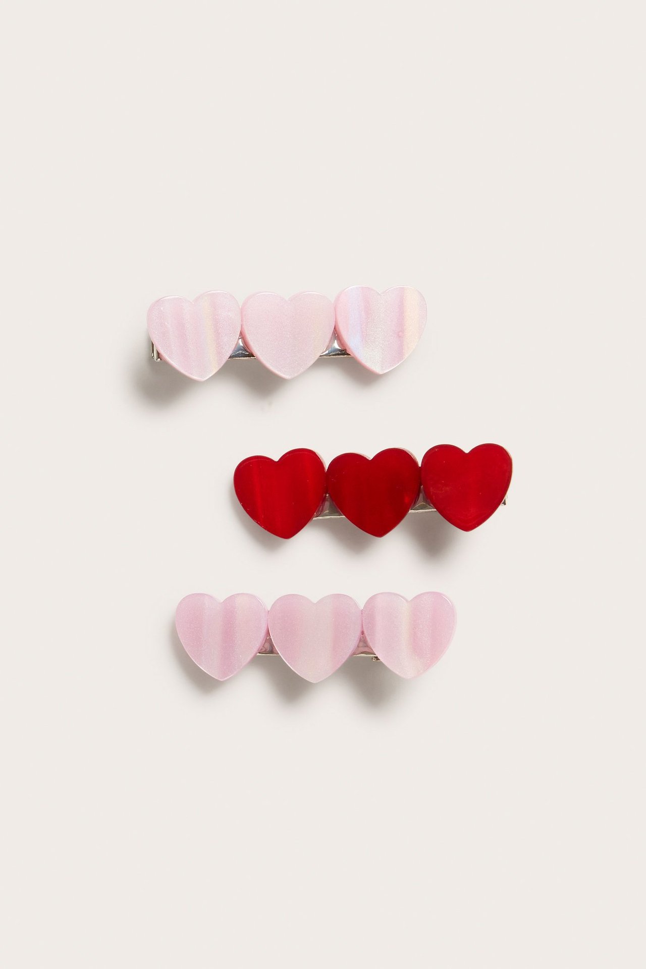 Zbliżenie 3-paku sercowatych plastikowych spinek do włosów, dwie jasnoróżowe opalizujące i jedna czerwona.