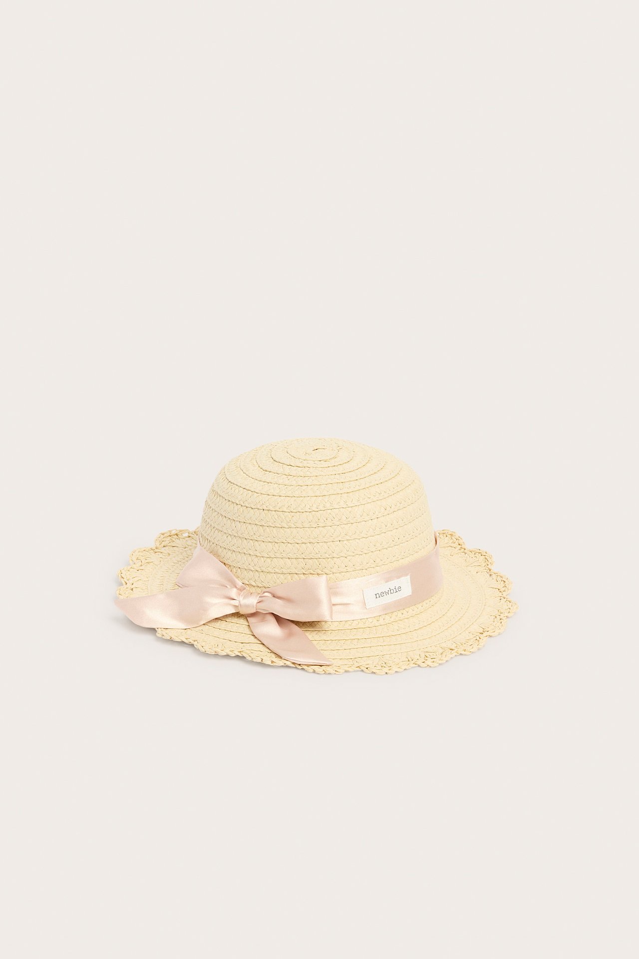 Frontvy av en ljusbeige stråhatt med en rosa satinrosett och vågig brätte.