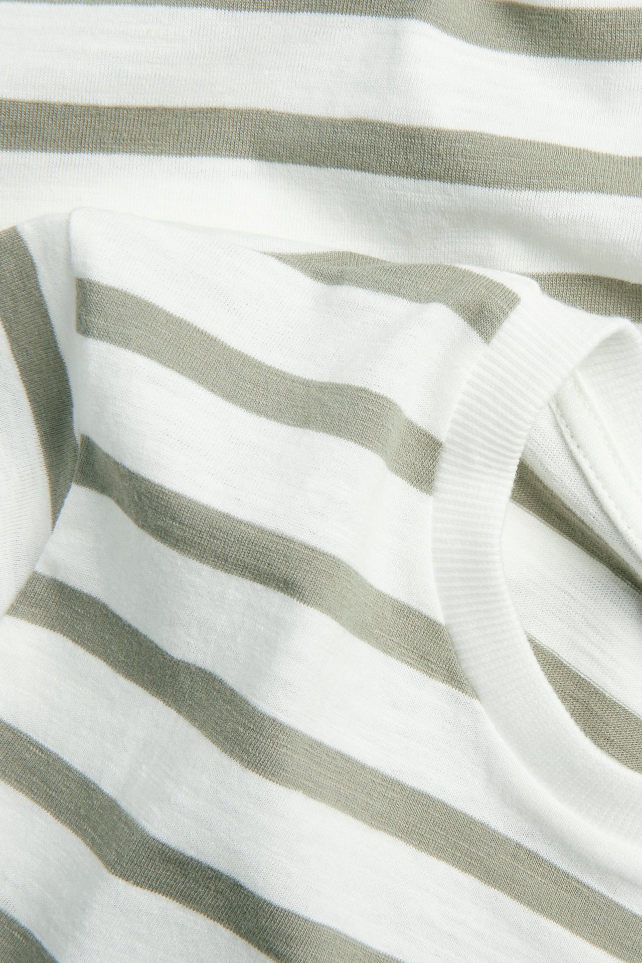 Zbliżenie na biały bawełniany t-shirt z ciemnozielonymi paskami i prążkowanym dekoltem.