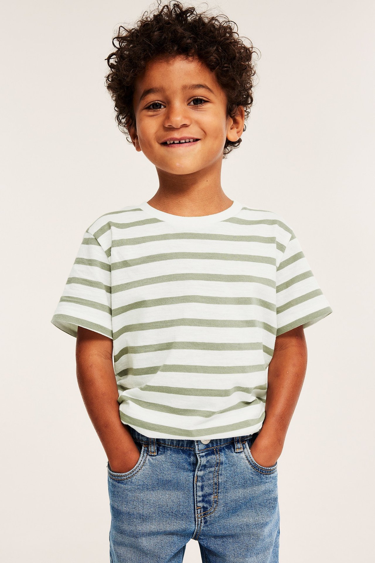 Framifrån: Ett barn bär en normal passform ljusgrön och vitrandig bomulls-t-shirt och blå jeans.