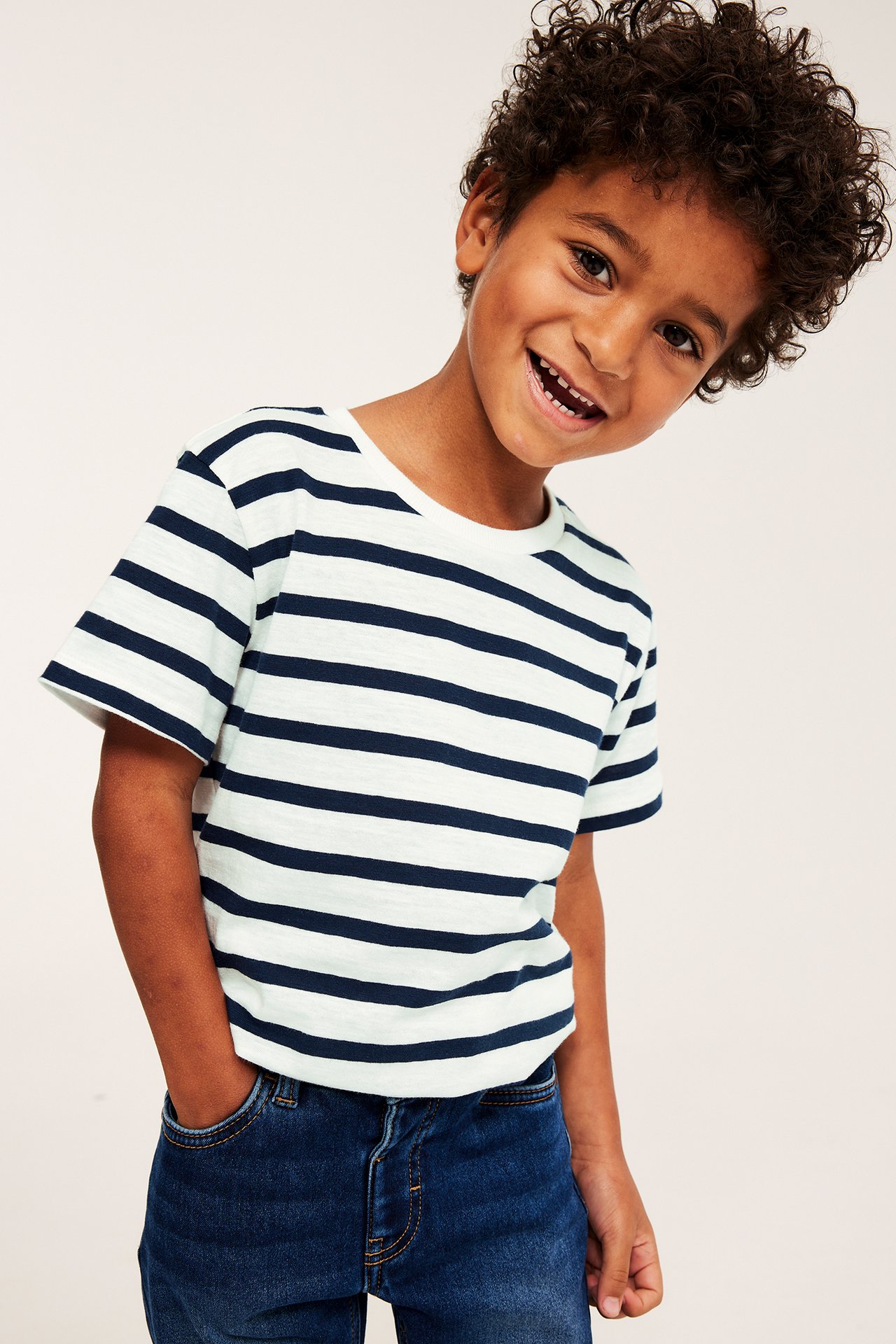 Framifrån: Ett barn bär en randig kortärmad t-shirt i mörkblå/ljus bomull, med mörkblå jeans.